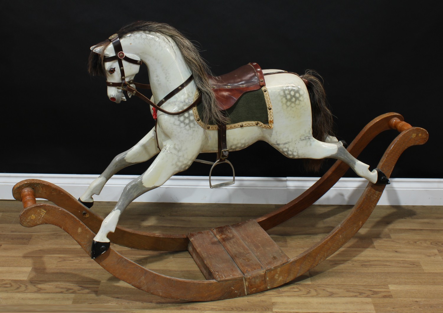 A good Edwardian dappled grey rocking horse on bow rockers, the carved, gesso and painted horse with pricked ears, flared nostrils, open mouth revealing carved teeth, the body with outstretched legs on a deeply curved elm rocker base with turned bails, real horse hair mane and tail, brown leather saddle and bridle, 146cm long, English c.1905