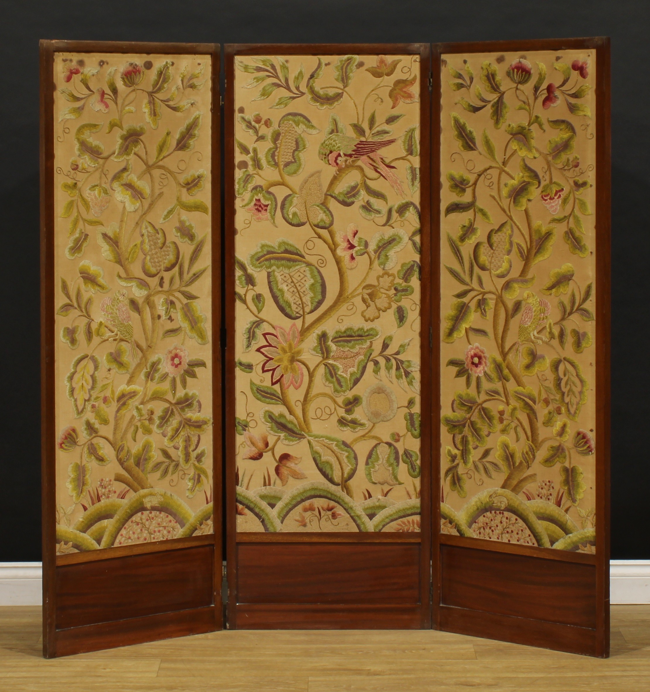 An Arts & Crafts period mahogany and woolwork three fold screen, worked in coloured threads with birds perched amongst flowering and fruiting stems, 153cm high, each panel frame 53.5cm wide, c.1910