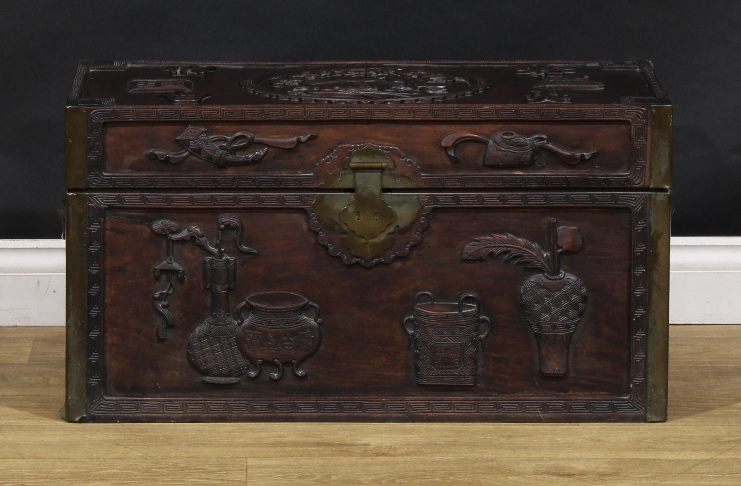 A Chinese hardwood rectangular chest, carved in relief with precious objects, characters and an elephant censer, carry handles to sides, 40cm high, 76cm wide, 40cm deep