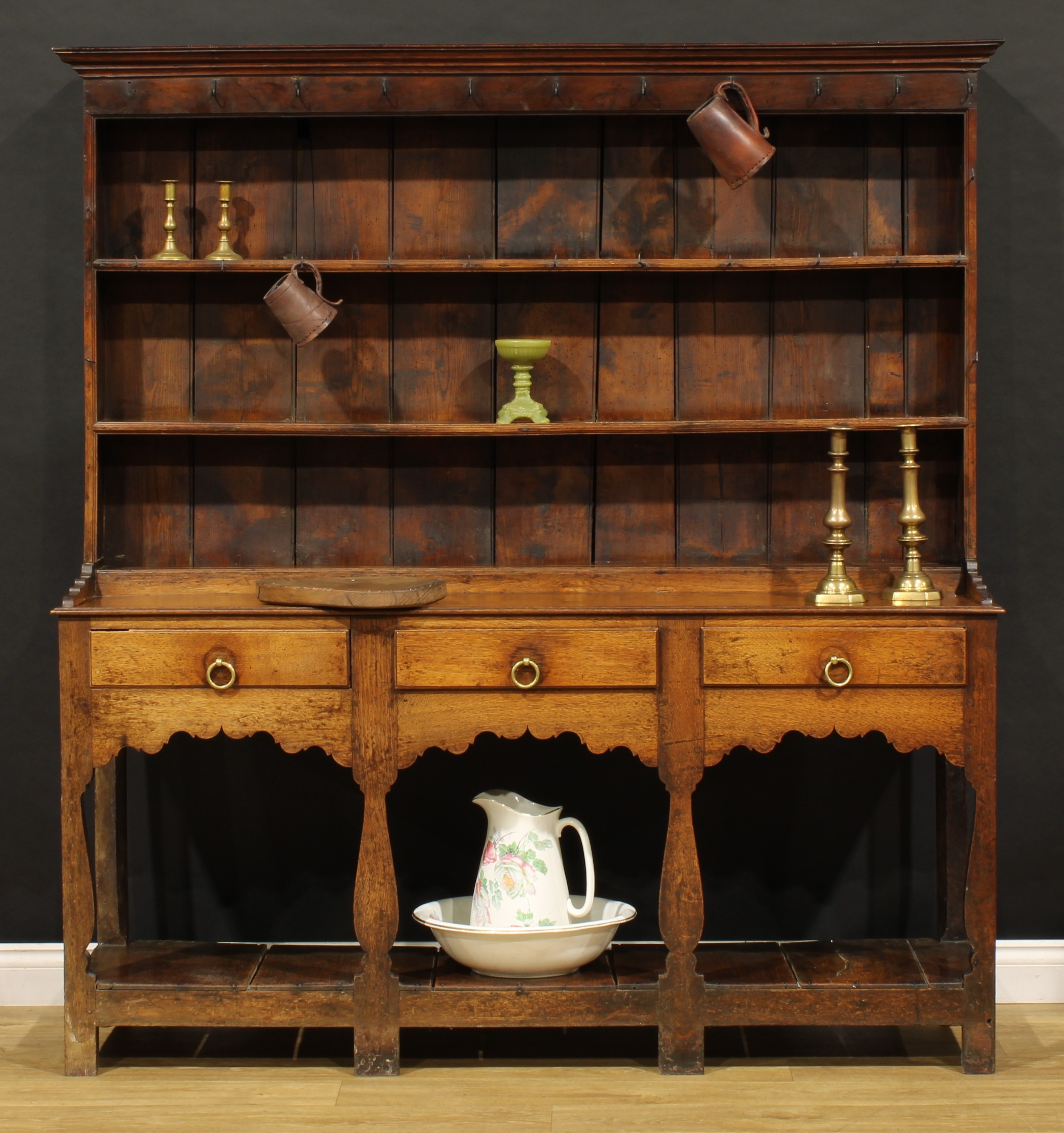 A George III oak pot board dresser, probably Welsh, the superstructure with two plate rack shelves and an arrangement of hooks, the projecting base with three frieze drawers, 180.5cm high, 171.5cm wide, 45cm deep, c.1810
