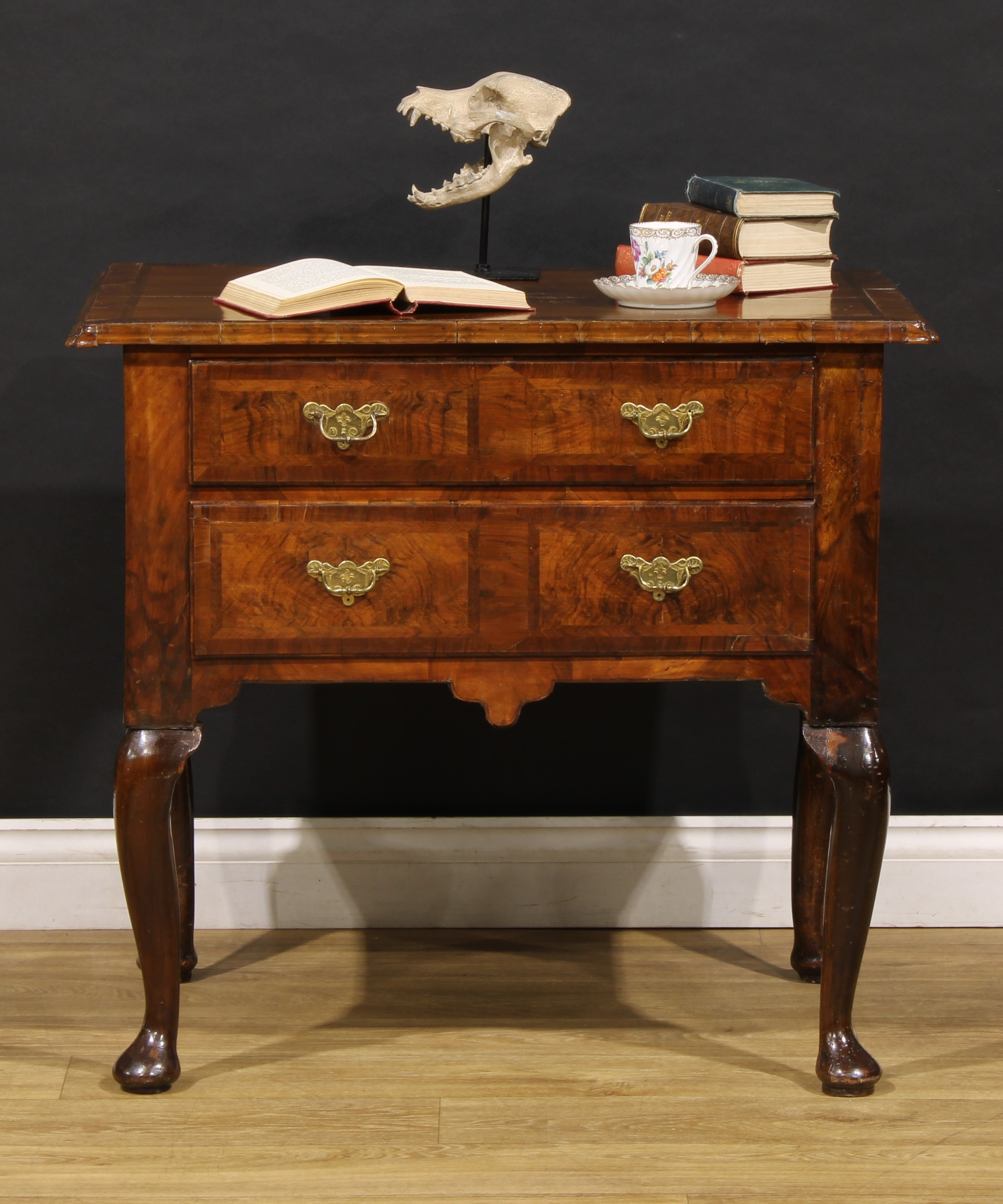 A George I walnut lowboy, moulded crossbanded quarter-veneered top above two long drawers, shaped apron, cabriole legs, pad feet, 76cm high, 82cm wide, 54cm deep, c.1725 with later additions and renovations