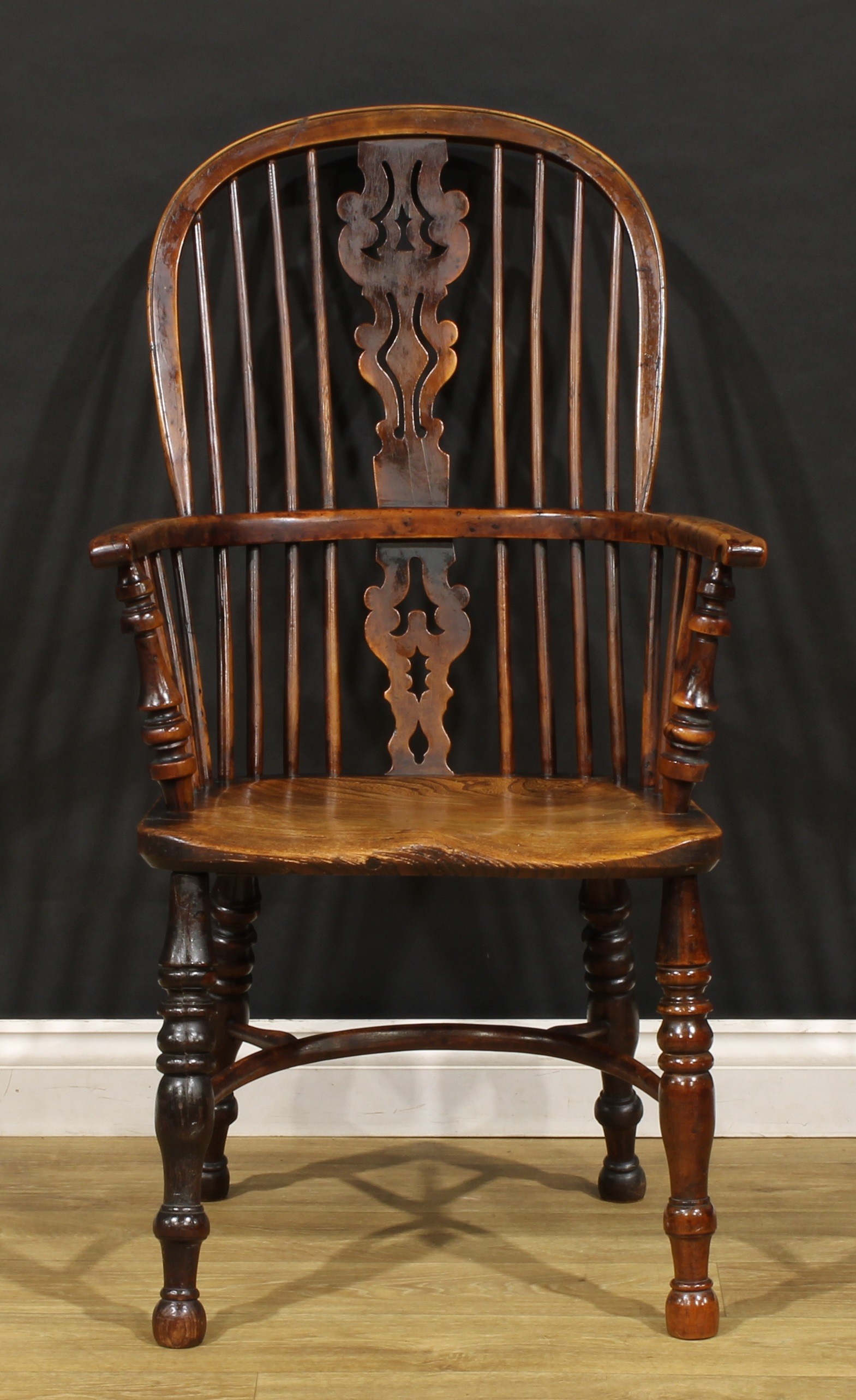A 19th century yew and elm Windsor elbow chair, hoop back, unusual splat shaped and pierced with a holly leaf, saddle seat, turned legs, crinoline stretcher, 105cm high, 59.5cm wide, the seat 42cm wide and 39cm deep, c.1820