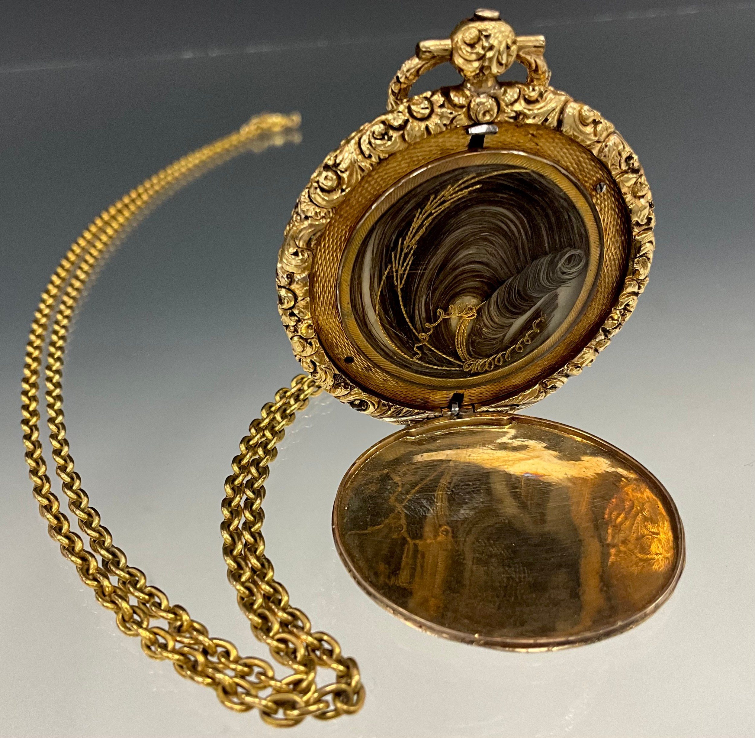 A Victorian yellow metal mourning locket, engine turned and floral decoration, the interior with hair and wire work panel, unmarked mount
