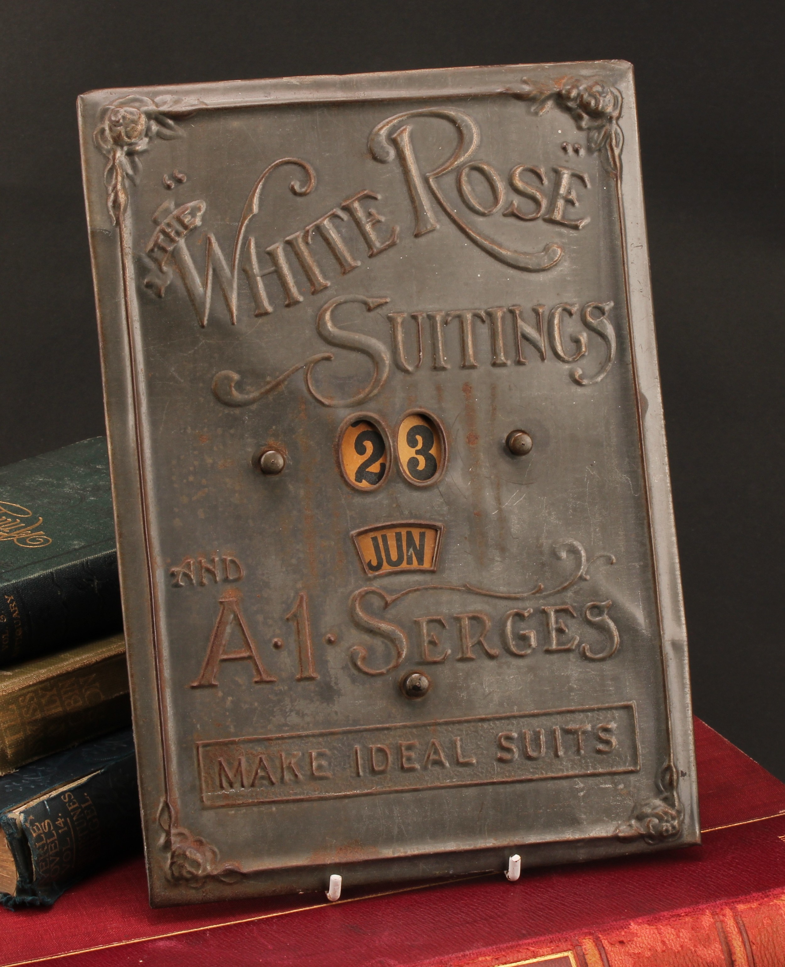 An early 20th century pressed tinplate perpetual calendar, The White Rose Suitings and A1 Serges
