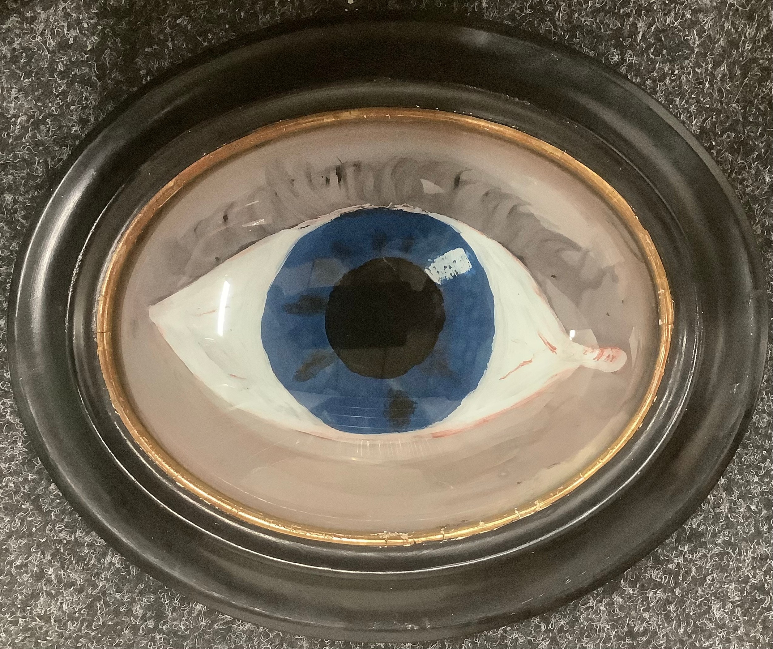 English School, an early 20th century reverse glass painting, of an eye, 33.5cm wide overall, ebonised frame