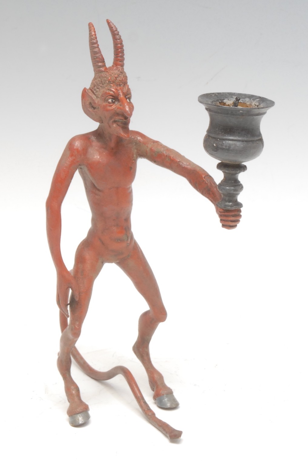 A 19th century cold-painted bronze figural candlestick, as a pagan devil with cloven hooves, he stands holding a campana sconce, 18.5cm high