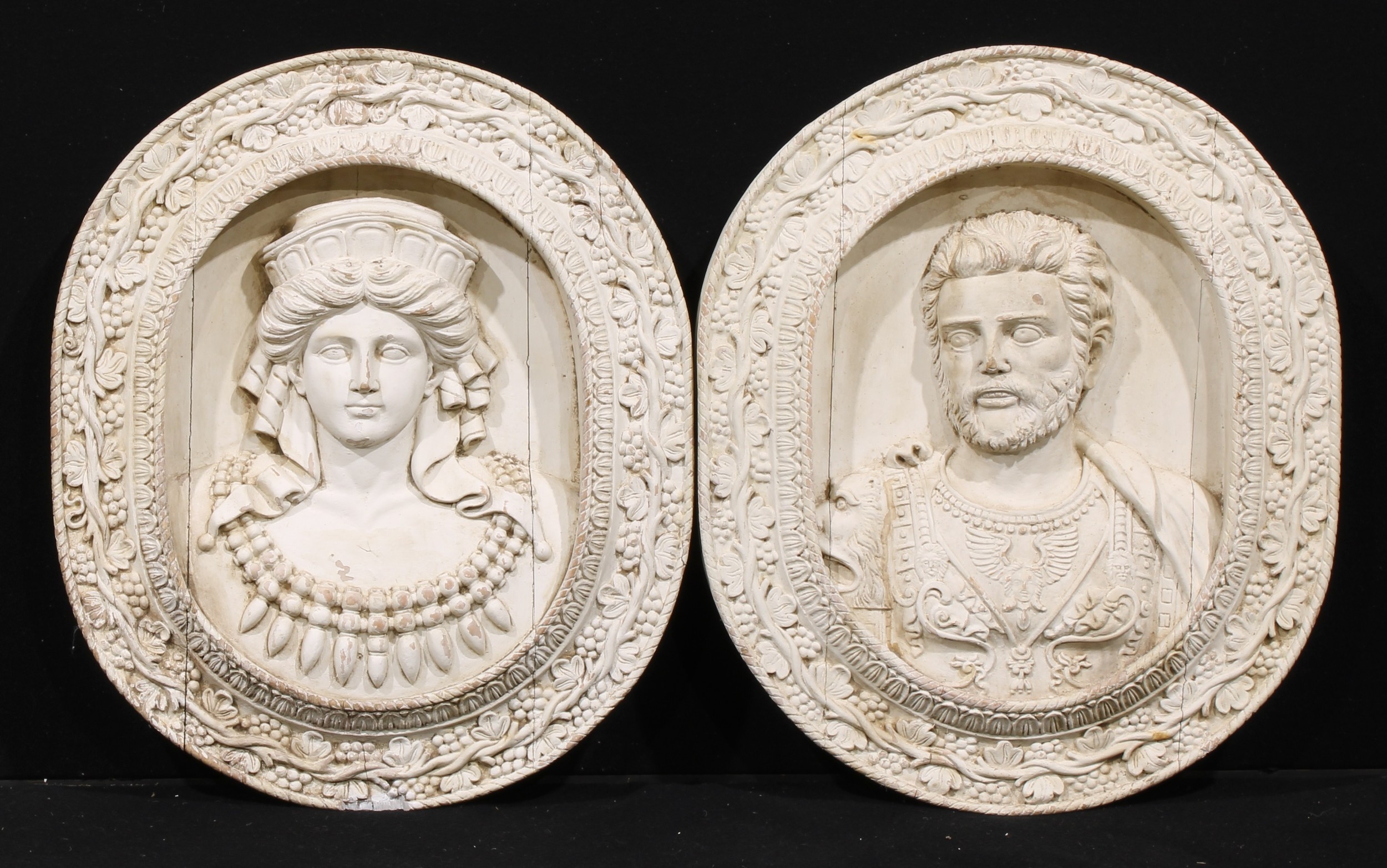 A pair of 19th century architectural softwood wall plaques, carved as Marcus Aurelius and Faustina the Younger, the frame carved and applied with fruiting vine, each 76.5cm high, 64cm wide, 8cm deep
