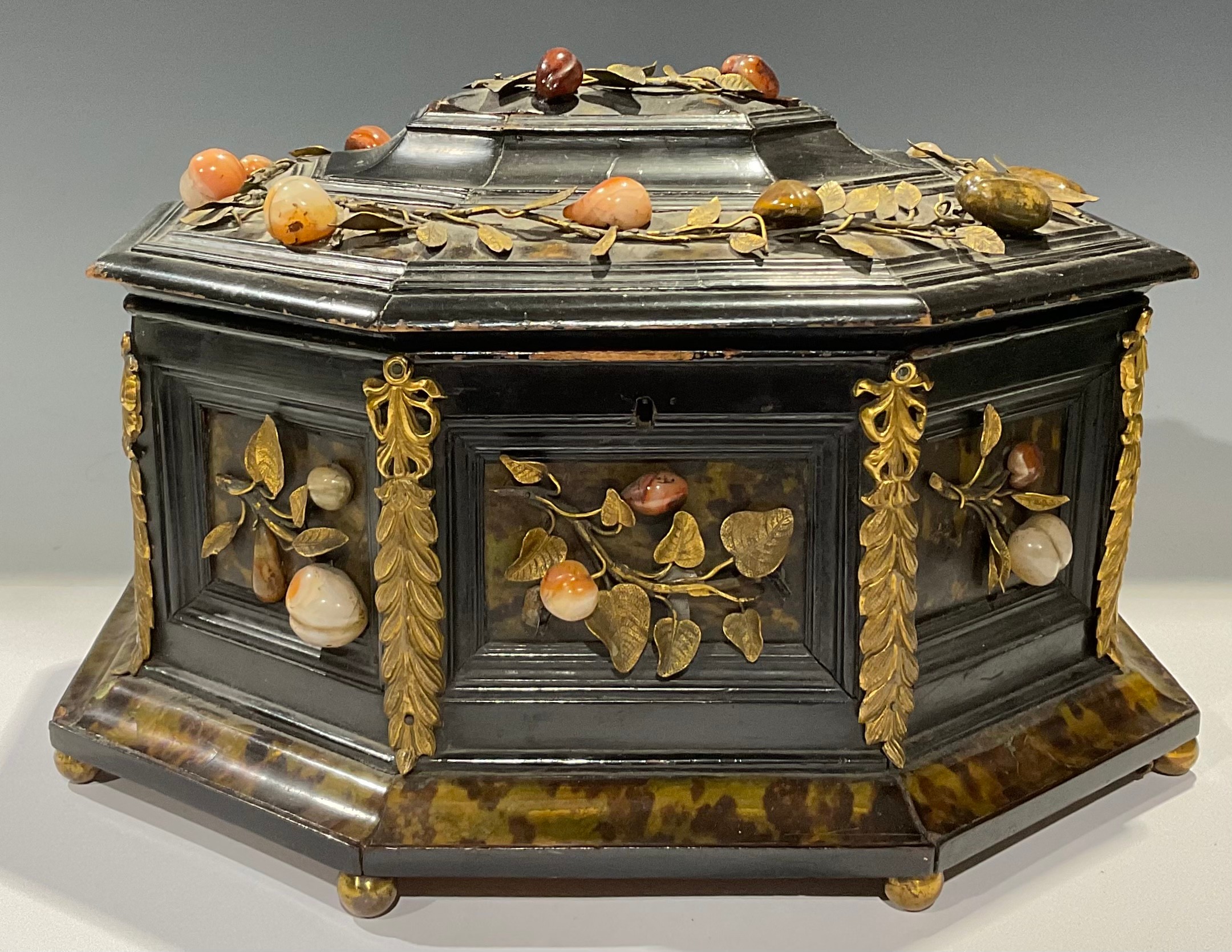 An Italian hardstone, gilt metal and tortoiseshell mounted canted rectangular table casket, sarcophagus cover enclosing a lift-out tray, carved and applied overall with ripe fruit on leafy branches, skirted base, ball feet, 35cm wide, 19th century