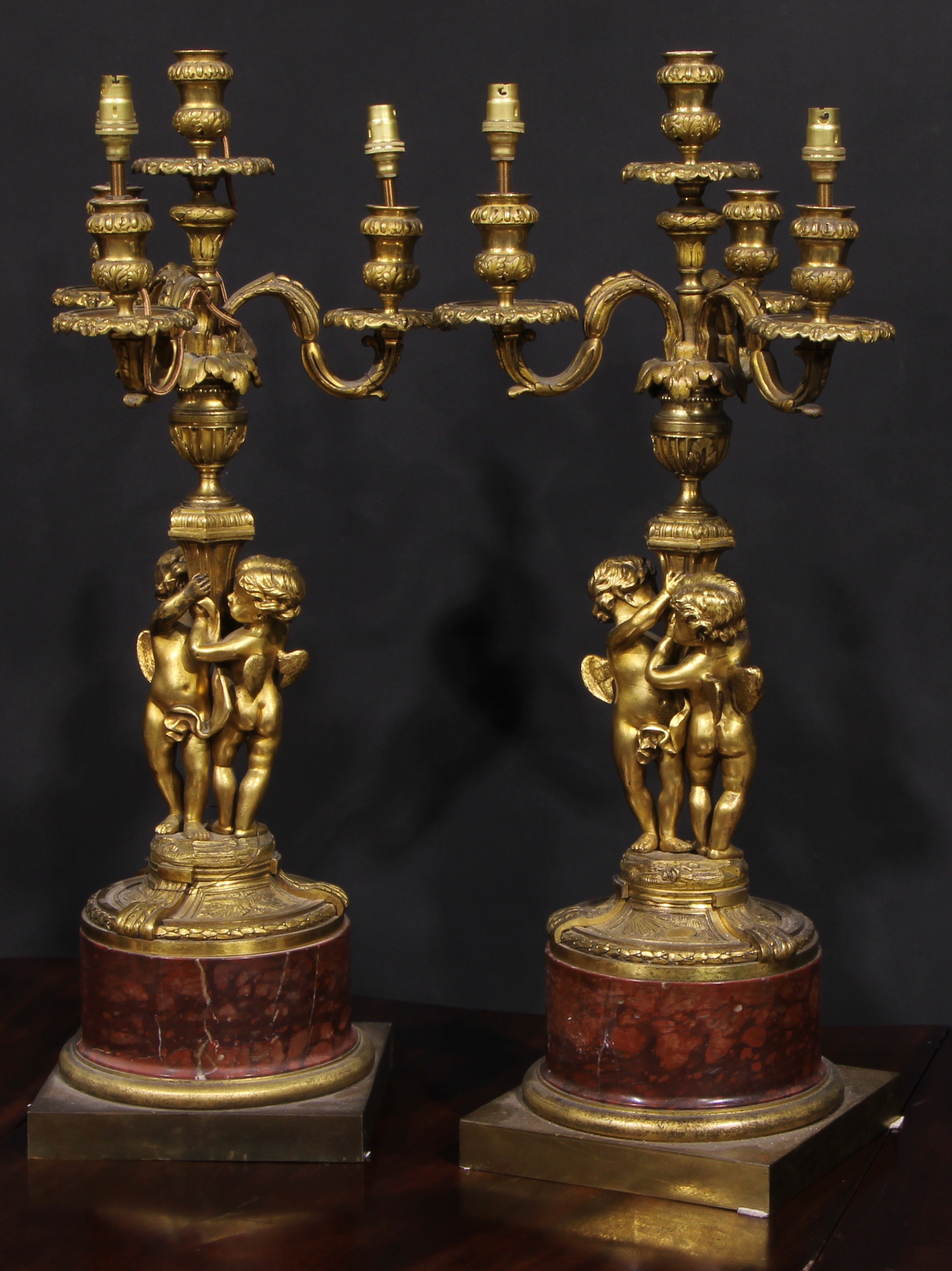 A pair of French gilt bronze figural five light candelabra, the pillars cast with putti, marble socles, square bases, 64cm high, early 20th century