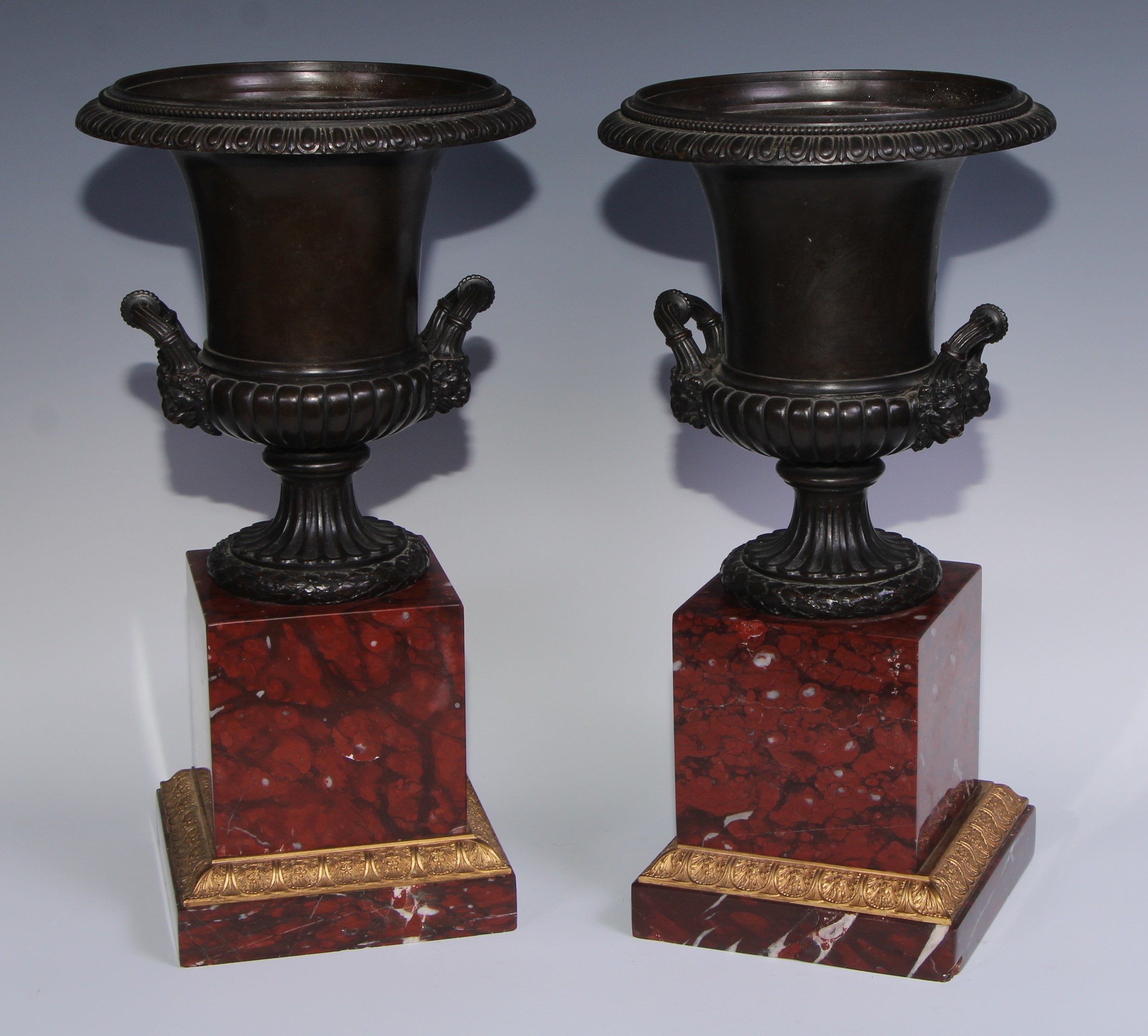 A pair of 19th century brown patinated bronze half-fluted campana urns, everted egg-and-dart rims, wrapped acanthus loop handles terminating in lion mask bosses, fruiting laurel bases, rosso antico marble plinths with gilt metal acanthus cast borders, 45cm high, c.1860
