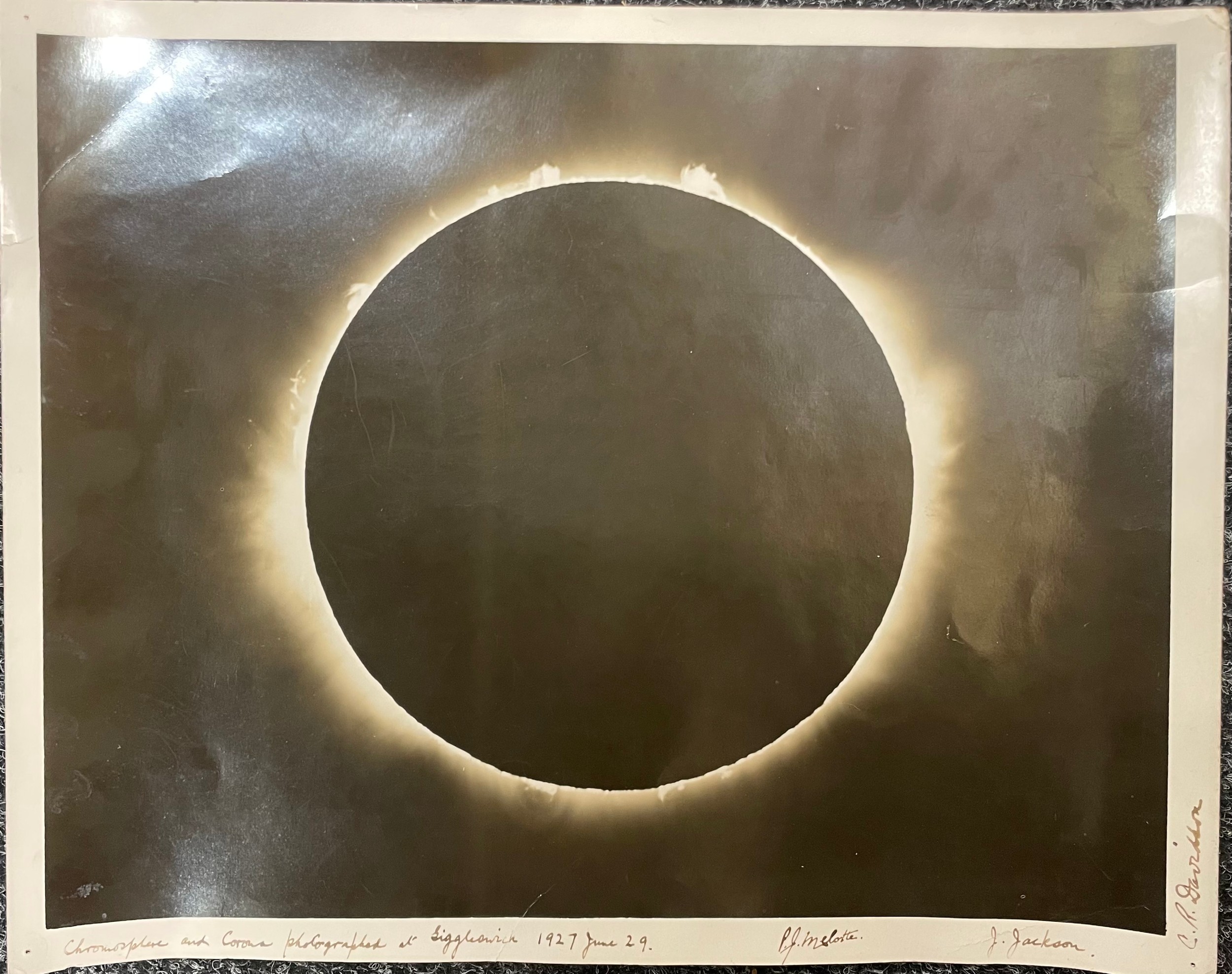 An original black and white photograph of the total solar eclipse, 29 June 1927, taken by John Jackson under direction of Sir Frank Watson Dyson, Astronomer Royal, at Giggleswick, North Yorkshire. Signed to the margins by three astronomers and Fellows of the Royal Astronomical Society: John Jackson, Charles Rundle Davidson, and Philibert Jacques Melotte. Inscribed, "Chromosphere and Corona photographed at Giggleswick 1927 June 29." This image, which captures the Sun's corona and prominences, was featured in The Times newspaper the following day, 30 June, where it was captioned 'the official photograph'. This was the first total eclipse to be visible from mainland Britain for 203 years, powerfully recorded in a diary entry by Virginia Woolf, 'We had fallen. It was extinct. There was no colour. The earth was dead.' [A Writer's Diary, Hogarth Press, 1953]. Gelatin silver print, 30.5 x 38cm. The image is remarkably well-preserved with some light creasing to corners, a marginal pin-hole at each corner, and a 1cm tear to left-hand margin, the verso has some light toning & handling marks with tape residue at top edge