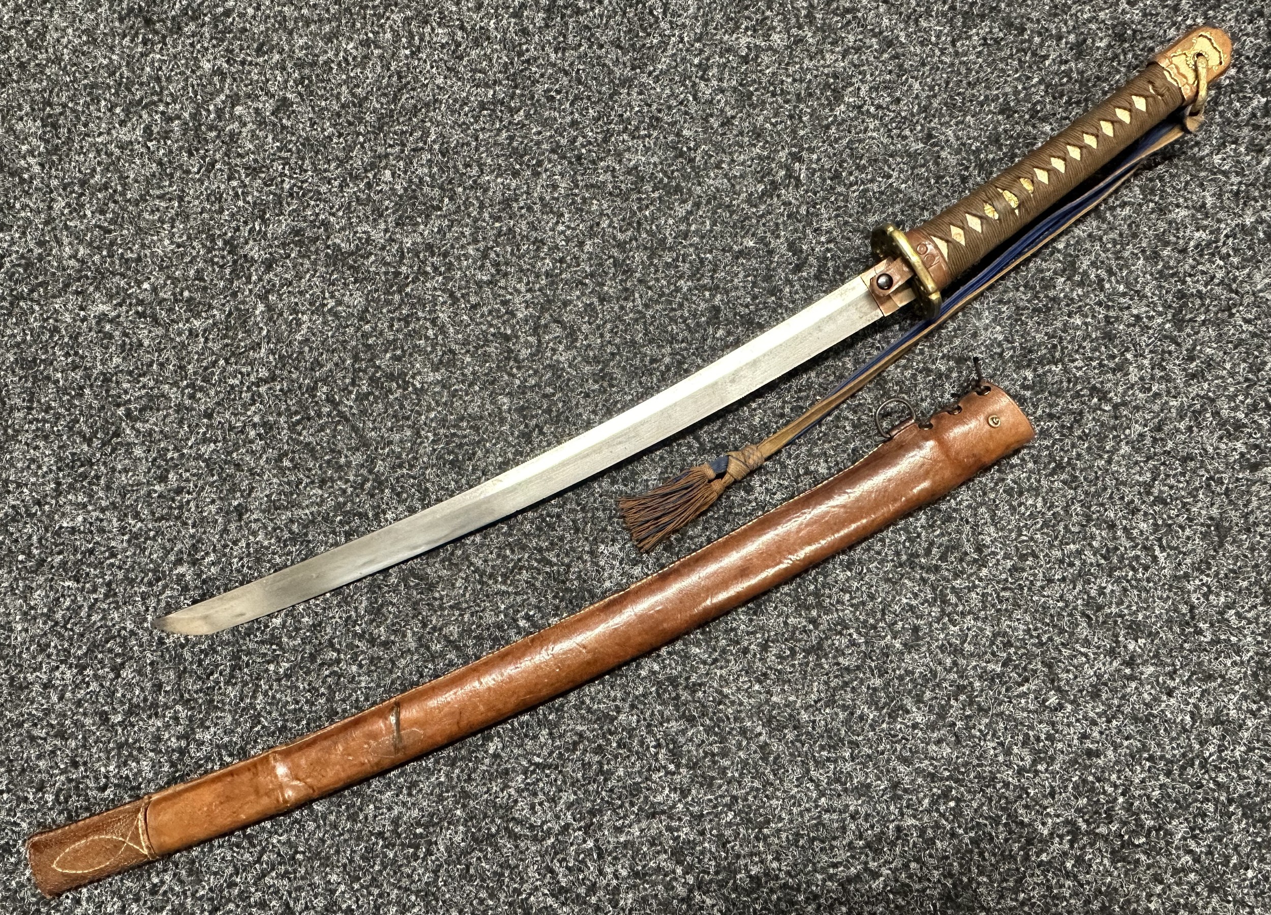 WW2 Japanese Officers Shin Gunto Katana Sword with single edged blade 535mm in length. Tang has two holes and is unsigned. Brass Tsuba. Overall length 770mm. Company Grade Officers Blue/Brown sword tassel. Brown leather covered Saya.