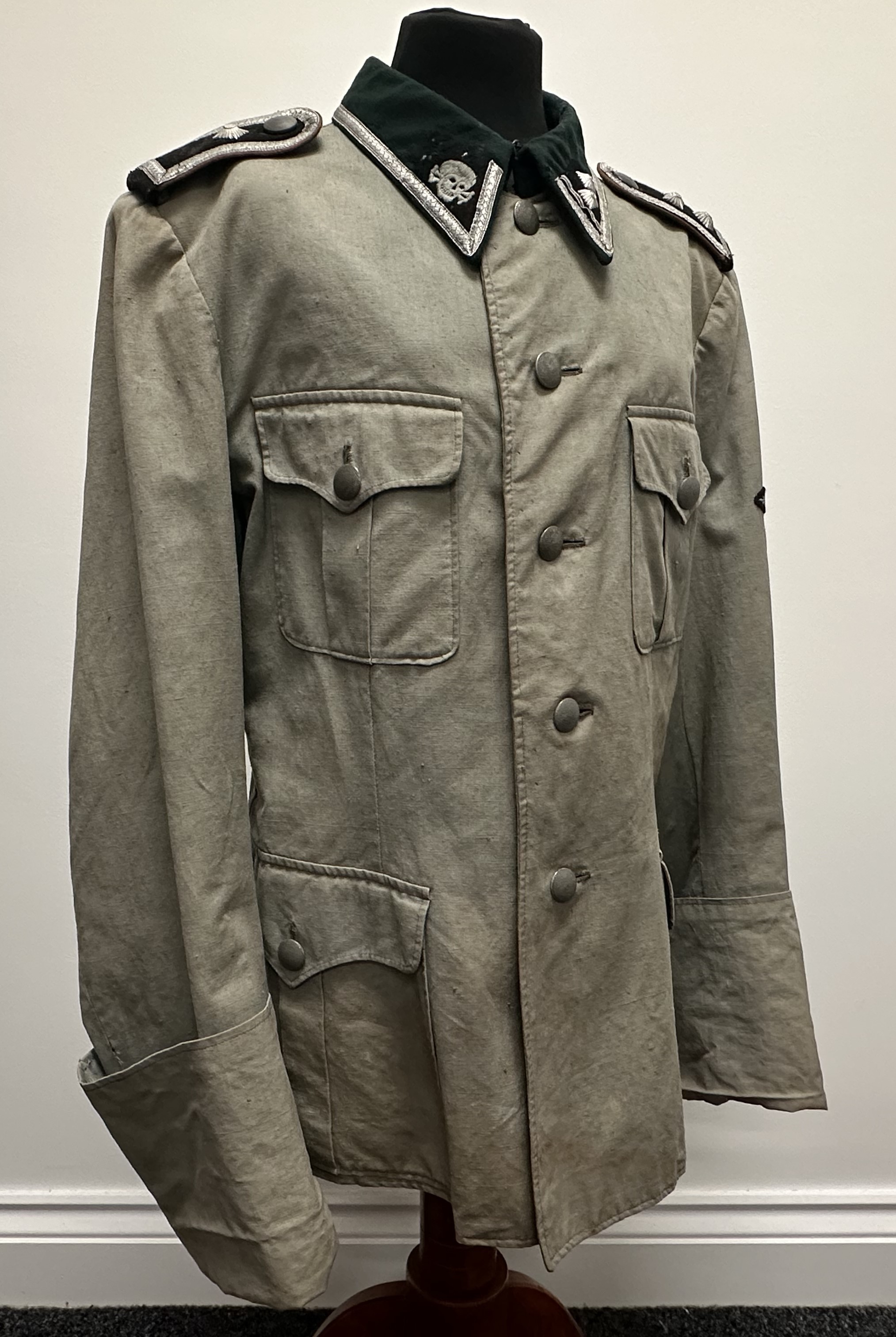 WW2 Rare Historically Significant Third Reich SS Totenkopfverbande privately custom tailored summer weight service tunic. Lightweight cotton material tailored in the style of a 1936 pattern tunic. Badge cloth faced collar with Totenkopf collar tab and rank tab for SS-Hauptscharführer. Shoulder straps piped in KZ Brown waffenfarbe. One rank pip missing for one strap. Sleeve eagle hand sewn with mothed wing tip. Tunic is very small size approx. 30 inch chest. No name or any markings. Sleeves are fully lined and the shoulders are padded. Part Rayon lining to shoulders. Underside of pocket flaps lined. Never had a cuff title. Provenance:  This item was obtain by a British Veteran of the 63rd Anti Tank Regiment Royal Artillery when his unit entered Bergen-Belsen Concentration Camp in April 1945.  Scanned photo shows the British Veteran wearing the tunic back home in Mansfield, Nottinghamshire in 1945. New to the market.