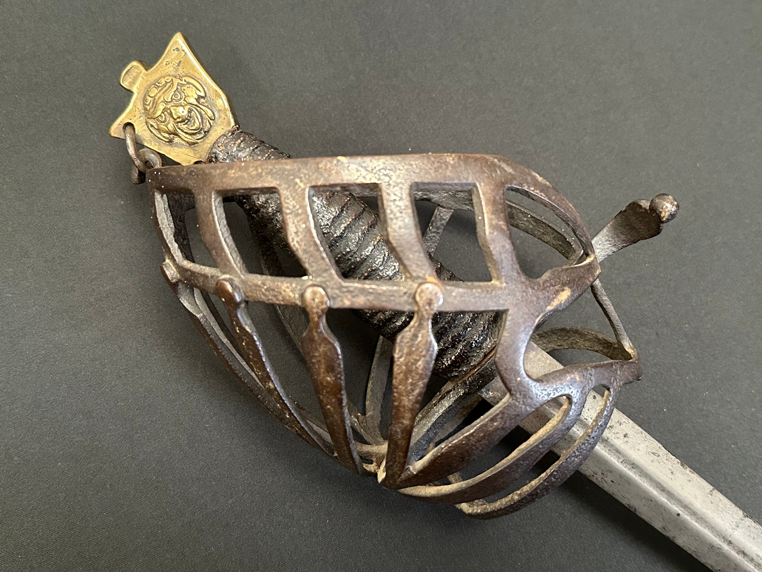 18th Century Italian Schiavona Half Basket-Hilt Sword with double edged blade with short fuller 900mm in length. No makers markings. Iron half basket with wooden grip with leather covering. Brass pommel with grotesque mask to both sides. Overall length 1057mm. No scabbard.