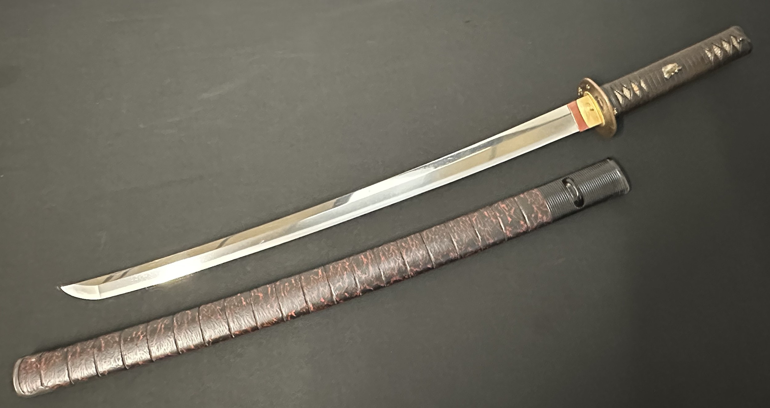 Japanese Sword with single edge blade 562mm in length. Good Hamon line. Tang in unsigned. Fish Menuki to grip. Overall length 742mm. Complete with a red & black lacquered Saya.