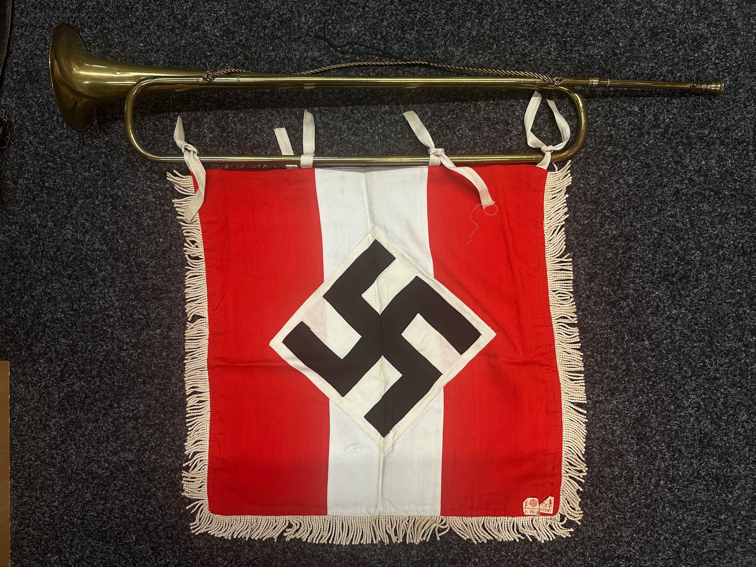 WW2 Third Reich HJ Trumpet and HJ Trumpet Banner. The trumpet is maker marked for "Sachs. Musik-Instrumenten Manufactur. Schuster & Co. Markneckirchen". With hanging cord. Banner has four tie tapes. White fringe to edges. Multipart construction and retains it's original RZM label sewn in place.