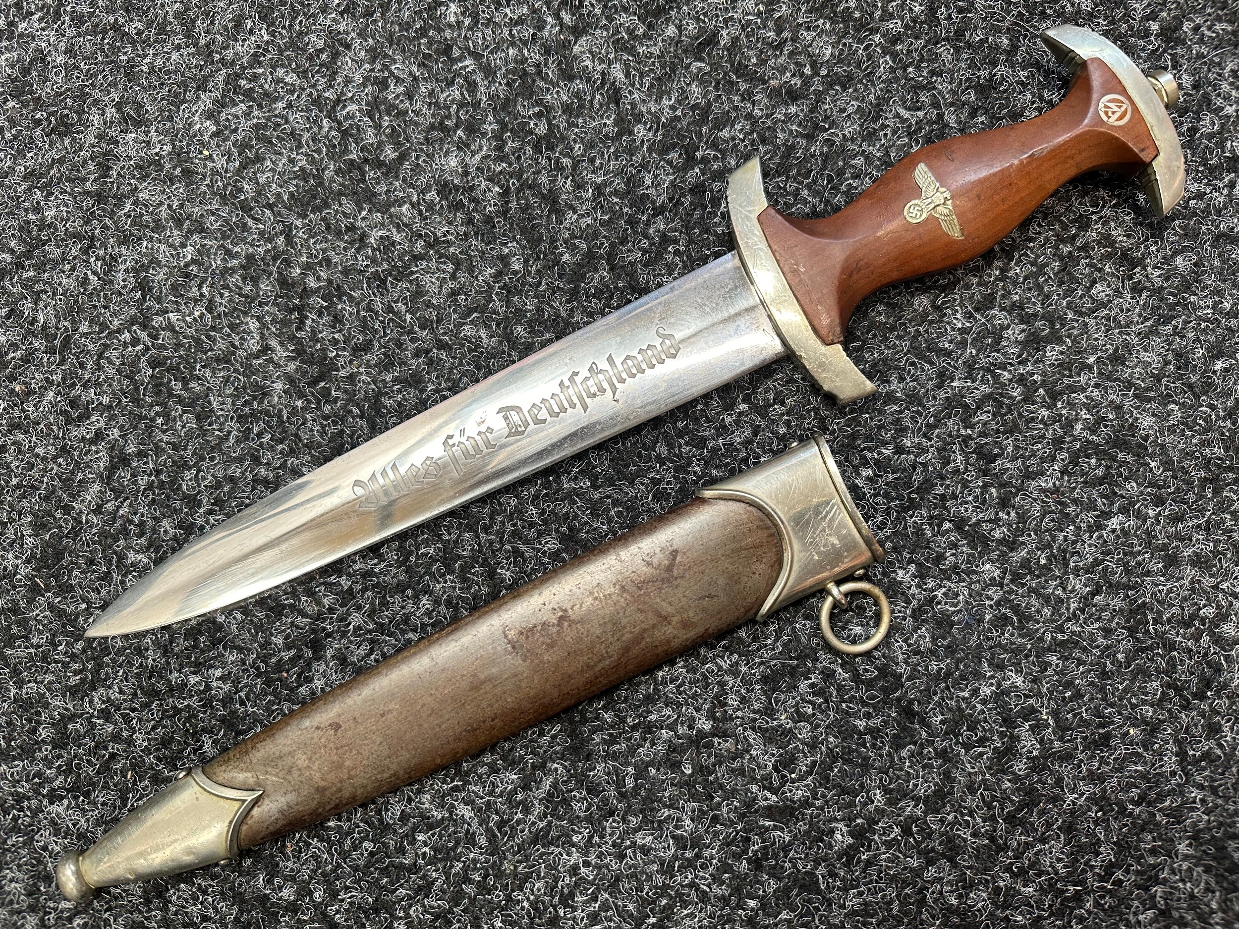 WW2 Third Reich SA Dienstdolch 1933 Pattern Dagger with double edged blade with "Alles Fur Deutschland" motto along with makers mark for "Hermann Schneider, Solingen-Aufderhone", 220mm in length. Early nickle fittings. Crossguard in SA Gruppe marked "NS" for Niedersachsen. Wooden grip complete with eagle and SA emblem. Overall length 345mm. Complete with scabbard with early annodised finish. War souvenir of a British Veteran of the 63rd Anti Tank Regiment Royal Artillery. New to the market.