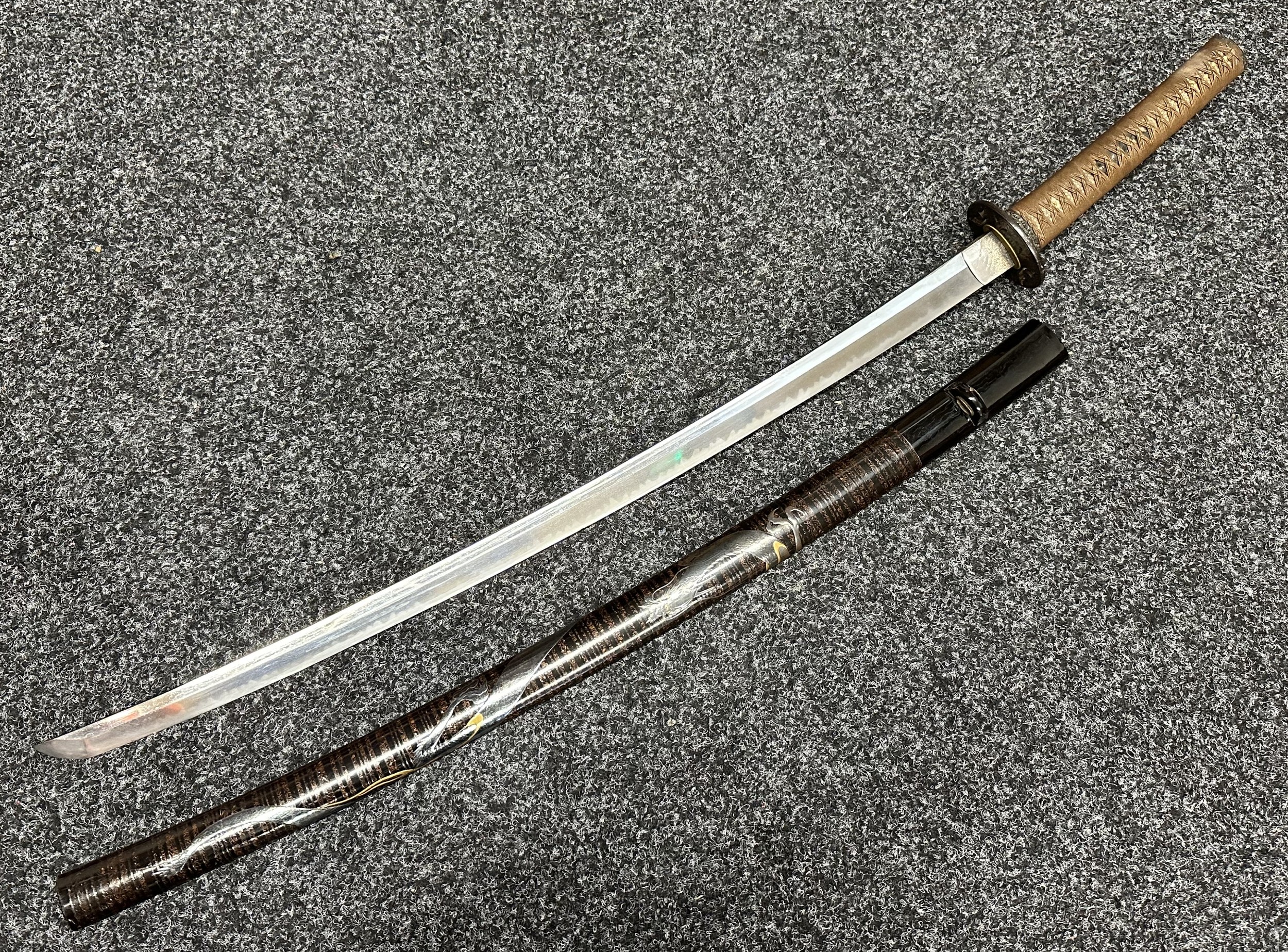 Japanese Sword with 730mm long single edged blade, good Hamon line. Unsigned tang. Iron tsuba. Rayskin covered grip with a Fish Menuki. Overall length 975mm. Lacquered wood saya decorated with a silver Dragon.