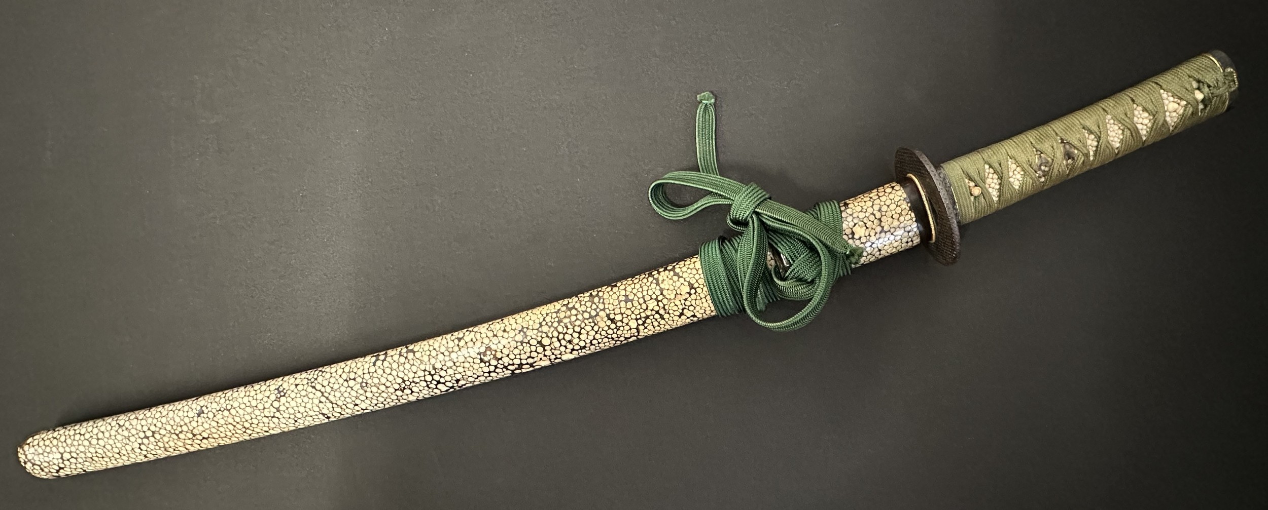 Japanese Wakizashi Sword with single edged blade 570mm in length. Hamon line to edge of blade. Tang is signed. Green cord binding to Rayskin grip. Menuki in the form of Deer. Overall length 733mm. Complete with Rayskin covered Saya which has some old labels. Fitted with a Kozuka knife with single edged blade 115mm in length. Unsigned. Overall length 212mm. Fitted with a green Sageo cord.