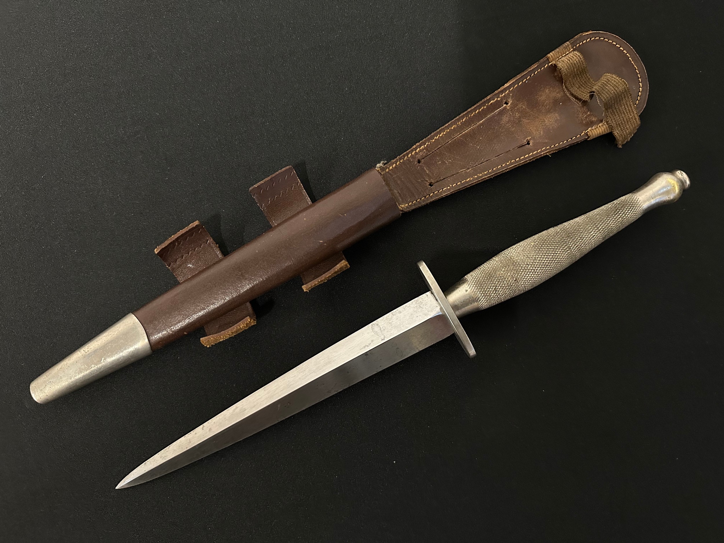WW2 British 2nd Pattern Fairbairn-Sykes Fighting Knife. Early Nickle finish knife with 169mm long blade. Crossguard is marked with a WD Broad Arrow & 5. Hand chequered grip. Overall length 297mm. Complete with early pattern scabbard with nickle finished chape. Both tabs to scabbard are present. Retaining elastic has split: New to the market with provenance. Original owner was Harry Holmes, Royal Engineers. Harry missed D-Day having picked up an injury playing football for his Regt. He  later fought in Normandy and North West Europe where he carried the knife.