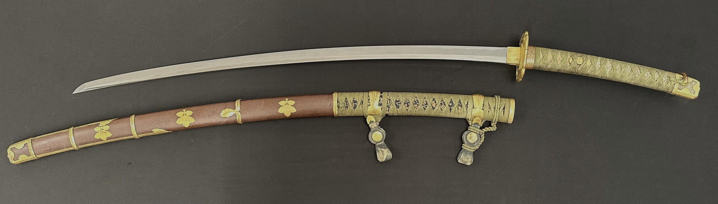 Japanese Katana Sword with single edged blade 755mm in length with Hamon line to the cutting edge. Tang is signed to both sides. Gilt habaki & inome-ni aoi-gata shape Tsuba. Samegawa Shagreen Ray Skin grip with green Tsuka-ito cloth binding with gilt Menuki. Overall length 1030mm. Complete with Saya scabbard in brown with matching fittings.