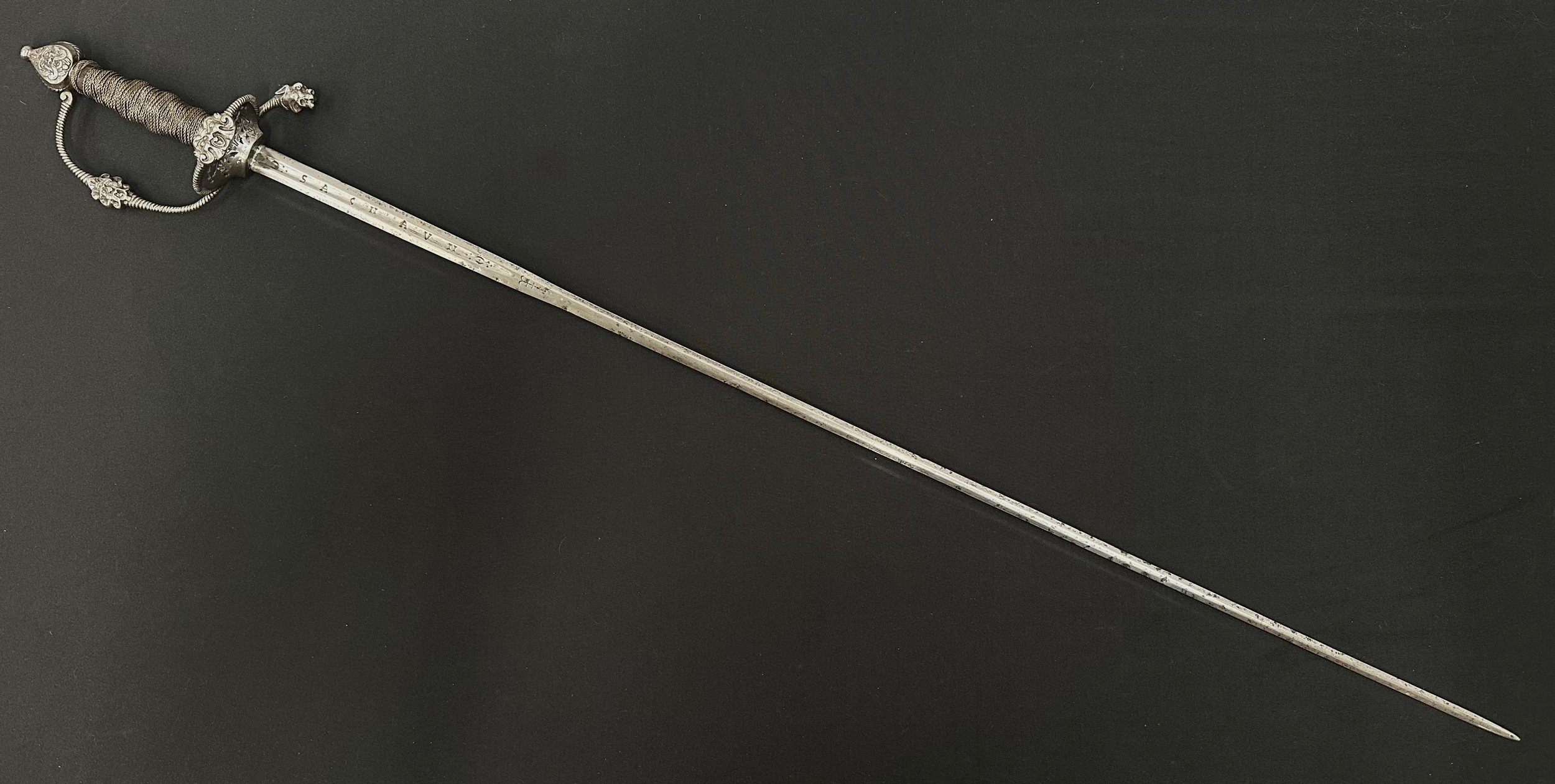 Rapier Sword with fullered double edged blade 792mm in length, marked "Sachav and "Eiviecho".  Guard with Lions head and Grotesque mask, pommel with grotesque mask. Wire bound grip. Brass accountability tag numbered "343" around grip. Overall length 940mm. No scabbard.