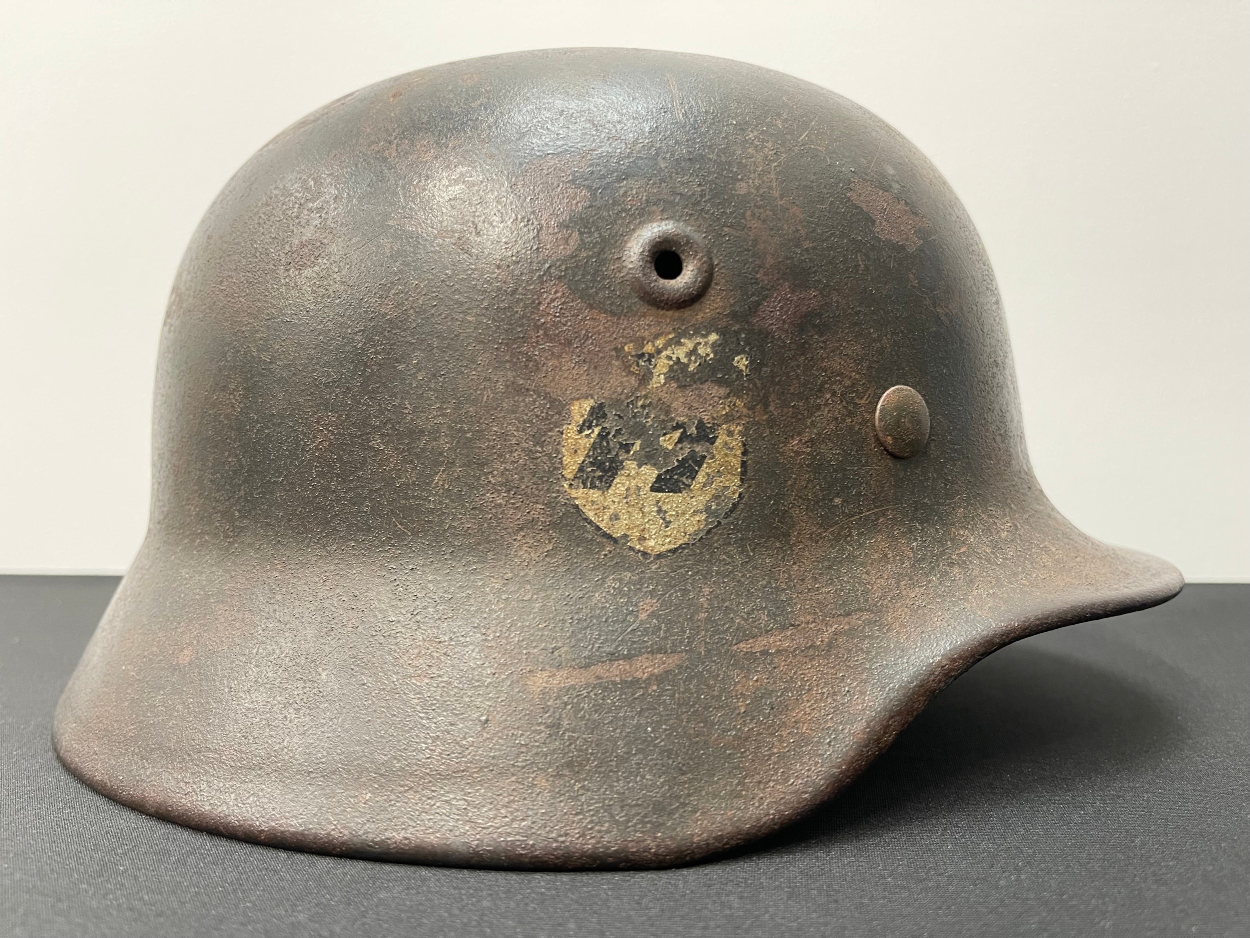 WW2 Third Reich Waffen SS Single Decal M40 Steel Helmet. Original feld grau paint. Original Q pattern SS Runic decal is approx 50% intact. Shell is marked with makers mark for Quist and size "Q62". Lot number to rear skirt of helmet appears to read "390". Liner is size "54". Original black leather chinstrap with steel buckle, no makers mark.