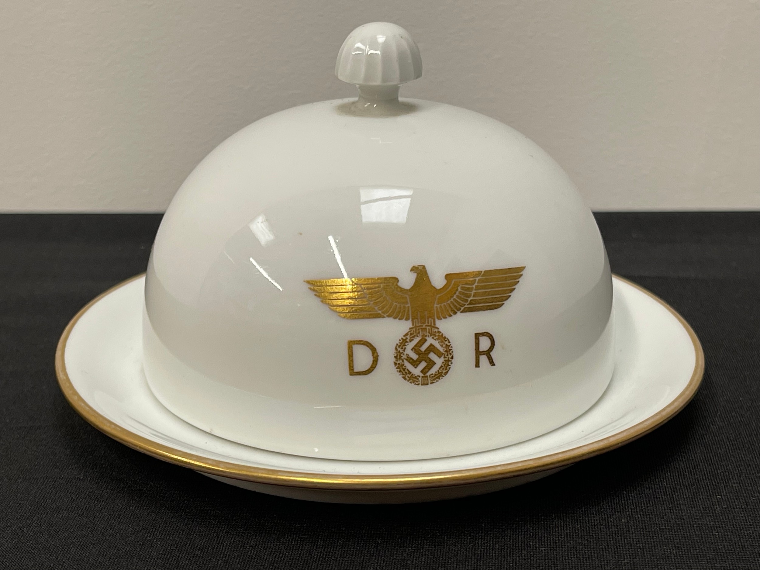 WW2 Third Reich Hermann Göring Nymphenburg Porcelain Domed Lidded Butter Dish From His Personal Deutsche Reichsbahn train Sonderzug "Asien" carriage number 10 205. Centered to the main body of the lid is the Deutsche Reichsbahn insignia of a gold eagle and swastika flanked by the letters D and R. To the underside of the dish is found the green Nymphenburg crest, an impressed Nymphenburg shield and a small inscribed  hand-painted number ‘205’ in black indicating the wagon number. Dish is 350mm in diameter. Overall height 84mm with lid in place.