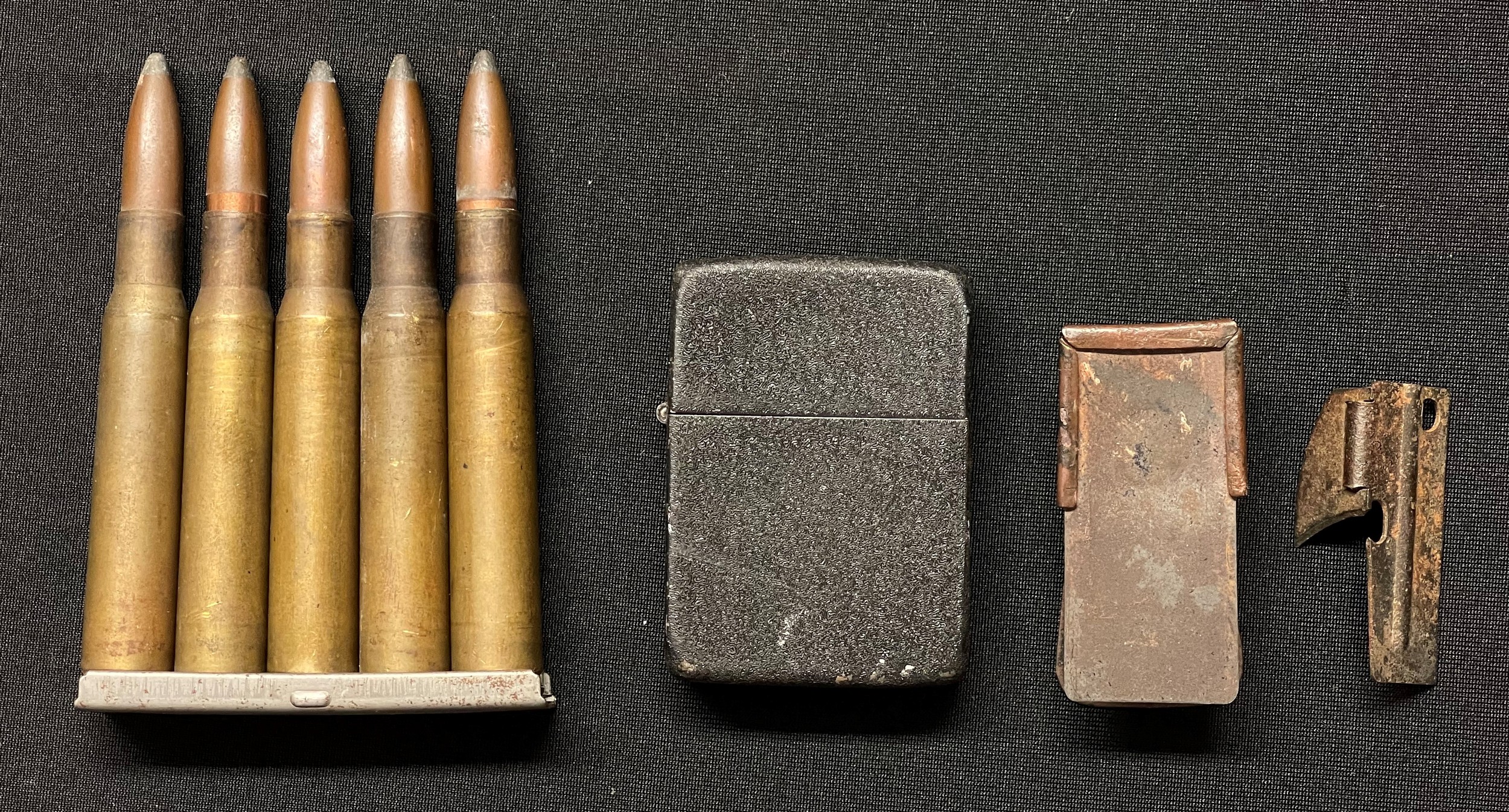 WW2 US Army Zippo Cigarette Lighter In Wartime Black Crinkle Finish: D-Day Airborne Cricket Clicker: P38 Ration Pack Tin Opener: Clip of five .30-06 INERT FFE Rounds all headstamped for Frankfurt Aresnal and dated 1941. Clip marked "SEY". (4)