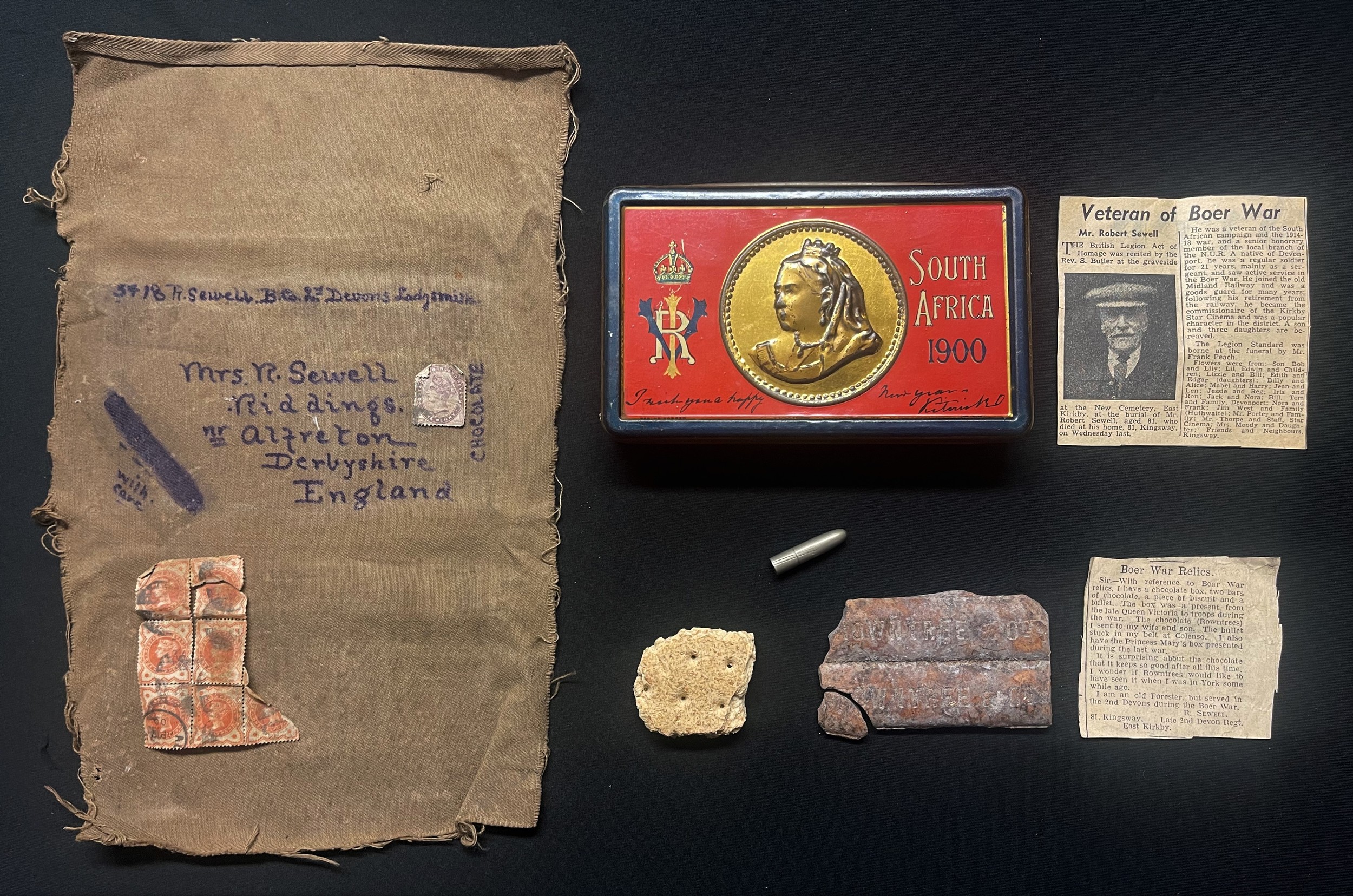 Boer War interest: Queen Victoria's South Africa 1900 Gift Tin which was issued to 3418 Pte Robert Sewell, 2nd Devons. He posted the tin home from Ladysmith to his wife wrapped in a khaki cloth cover. The tin has inside it two bars of the original Rowntrees chocolate and a biscuit in addition to a Boer bullet which struck Pte Sewells belt at the Battle of Colenso in 1899. There is also a Newspaper cutting citing a letter about the tin and contents written by Mr Sewell plus another newspaper cutting with his Obitury.