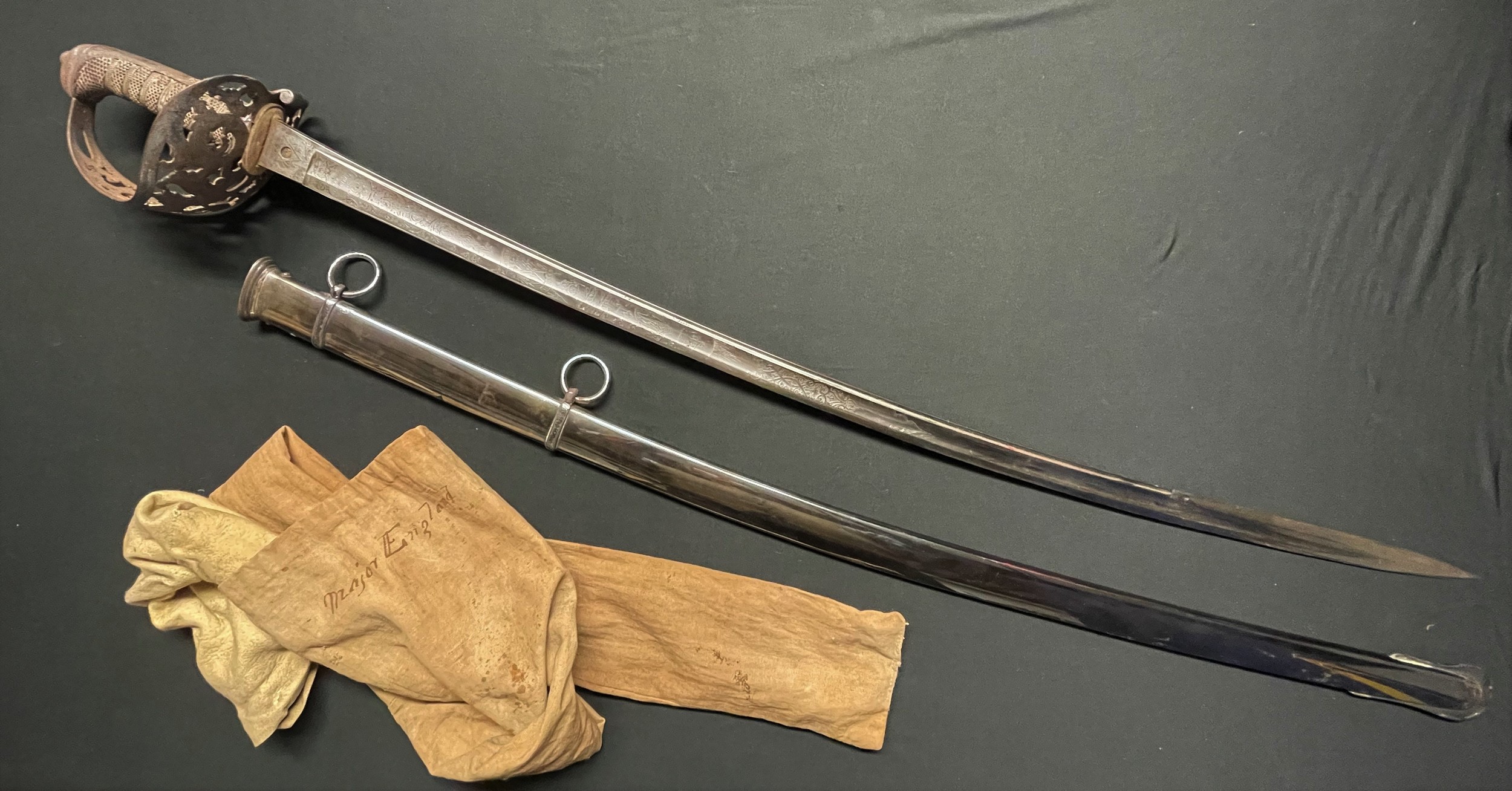 British Victorian X Lancers Cavalry Officers Sword with fullered curved blade 890mm in length with etched decoration to both sides with battle honours, VR and Queens Crown, Proof marked along with makers mark for Henry Wilkinson, Pall Mall, London. Spine of blade numbered 14811. Felt washer still in place. Wire bound grip. Overall length 105cm. Complete with plated scabbard with twin suspension rings. In addition it has a chamois leather cover and a cloth cover. Cover is named to "Major England". NOTE: Major England's medals also feature in this sale as lot 3000.