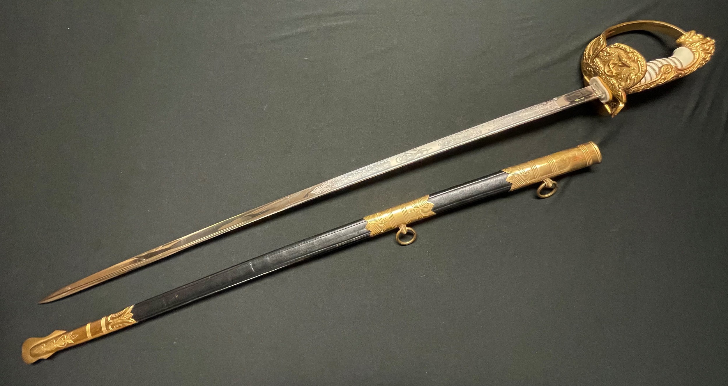 Kreigsmarine Officers Lion Head Sword with pipe backed blade 810mm in length with etched decoration of sailing ships, foliage and anchor to one side, the other side having foliage, sailing ship and naval trophy with trident to centre. Blade has makers trade mark of "E & F Horster Solingen". Fine white celluloid grip retaining the original wire binding. Gilt folding guard with central anchor, guard with fine relief, leading to the lion head pommel having set with green and red (port and starboard) jewelled eyes. Ferrule in the form of a band of oak leaves. Plain folding rear catch. Overall length 950mm. Complete with leather and brass mounted scabbard with two suspension rings