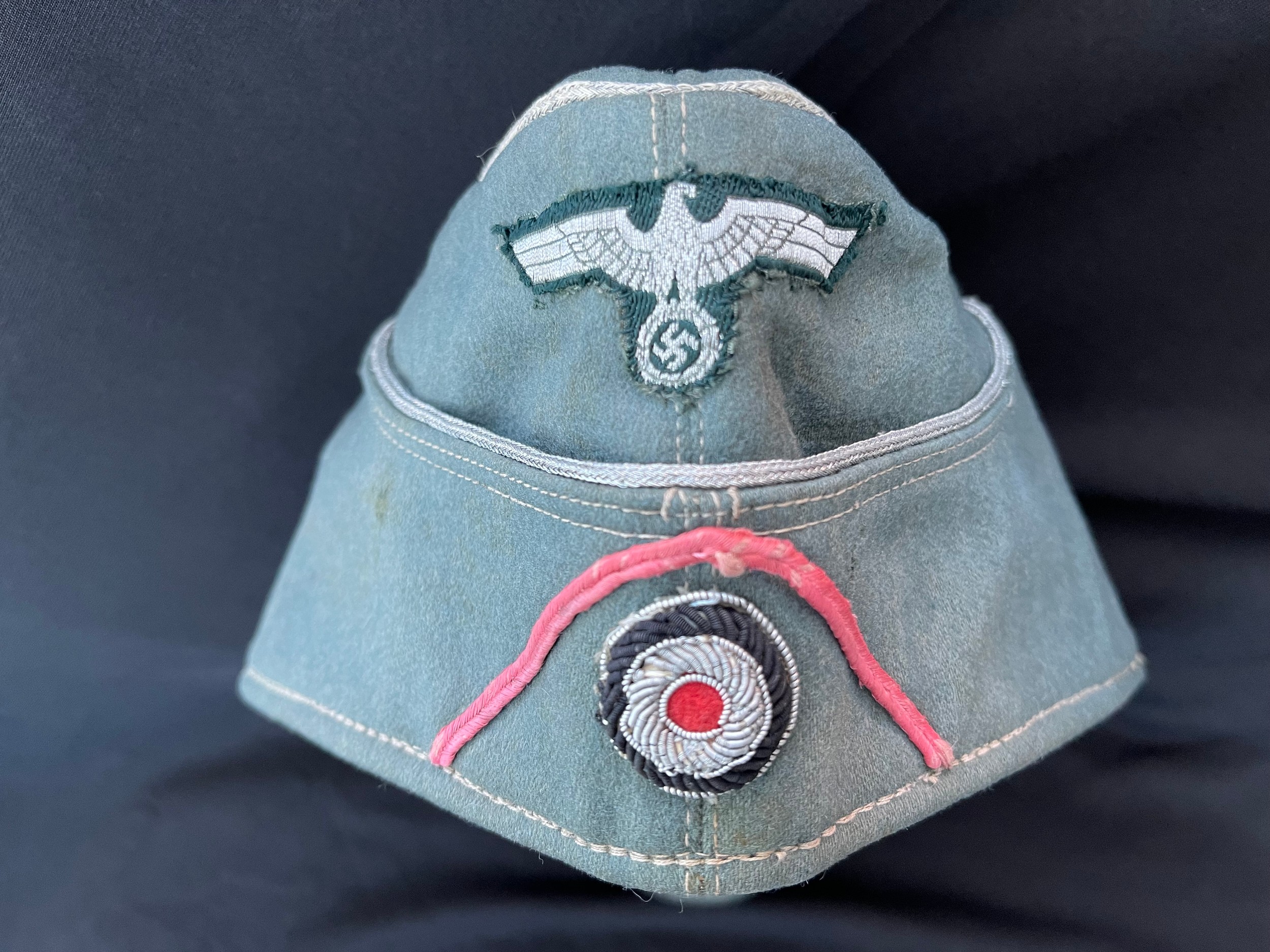 WW2 Third Reich Heer Officers M38 Feldmutze in fine doe skin wool. Early war dark green backed Bevo machine woven flatwire eagle. Bullion embroidered national cockade. Silver wire pipred. Panzer Pink Soutach. Size 57. Cotton lined with partial grey leather sweatband marked "Qualitats Marke". Zink air vents. Field repair to rear of cap.