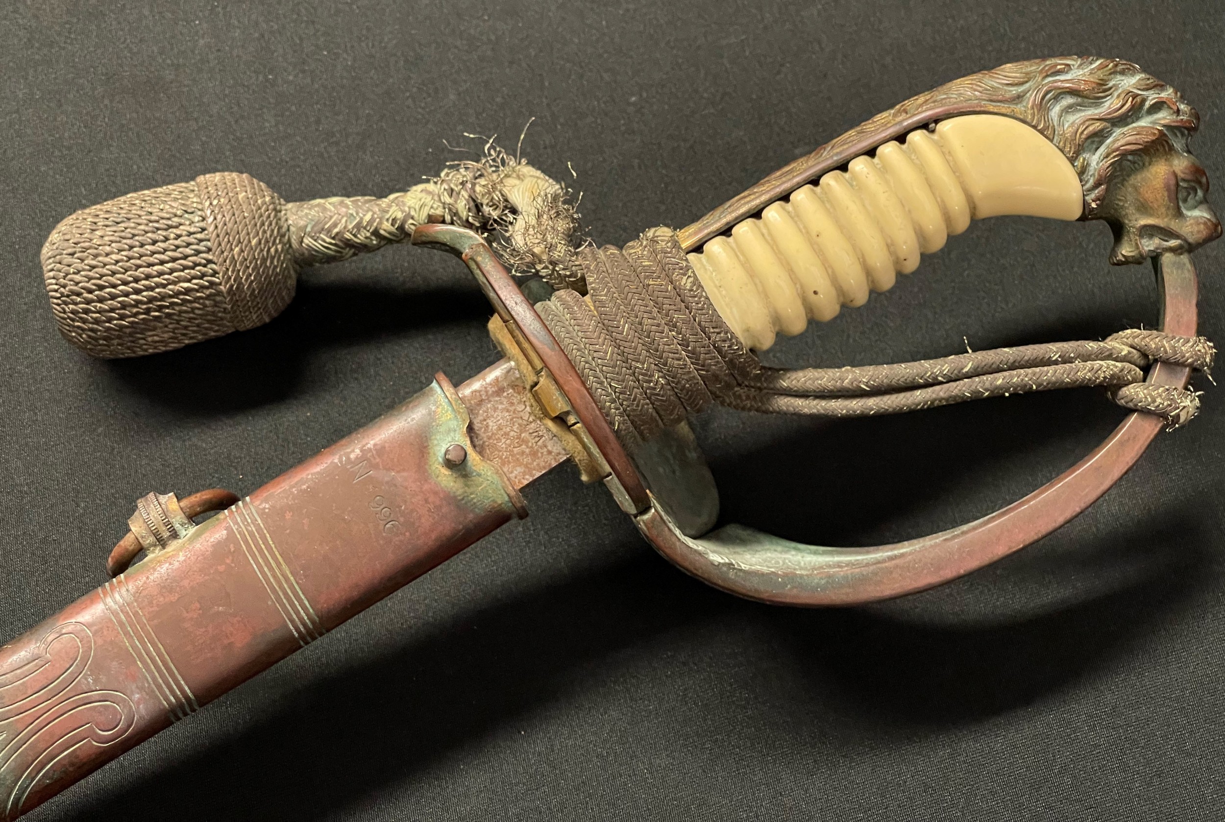 WW2 Third Reich Kreigsmarine Officers Lion Head Sword with pipe backed blade 695mm in length. Maker marked "WKC". Felt washer present. Folding guard marked with Eagle M inspection mark along with N1966. White celluloid grip, missing grip wire. Lions Head Pommel. Complete with original knot. Overall length 830mm. Complete with leather scabbard with matching numbers, brass fittings and twin suspension rings.