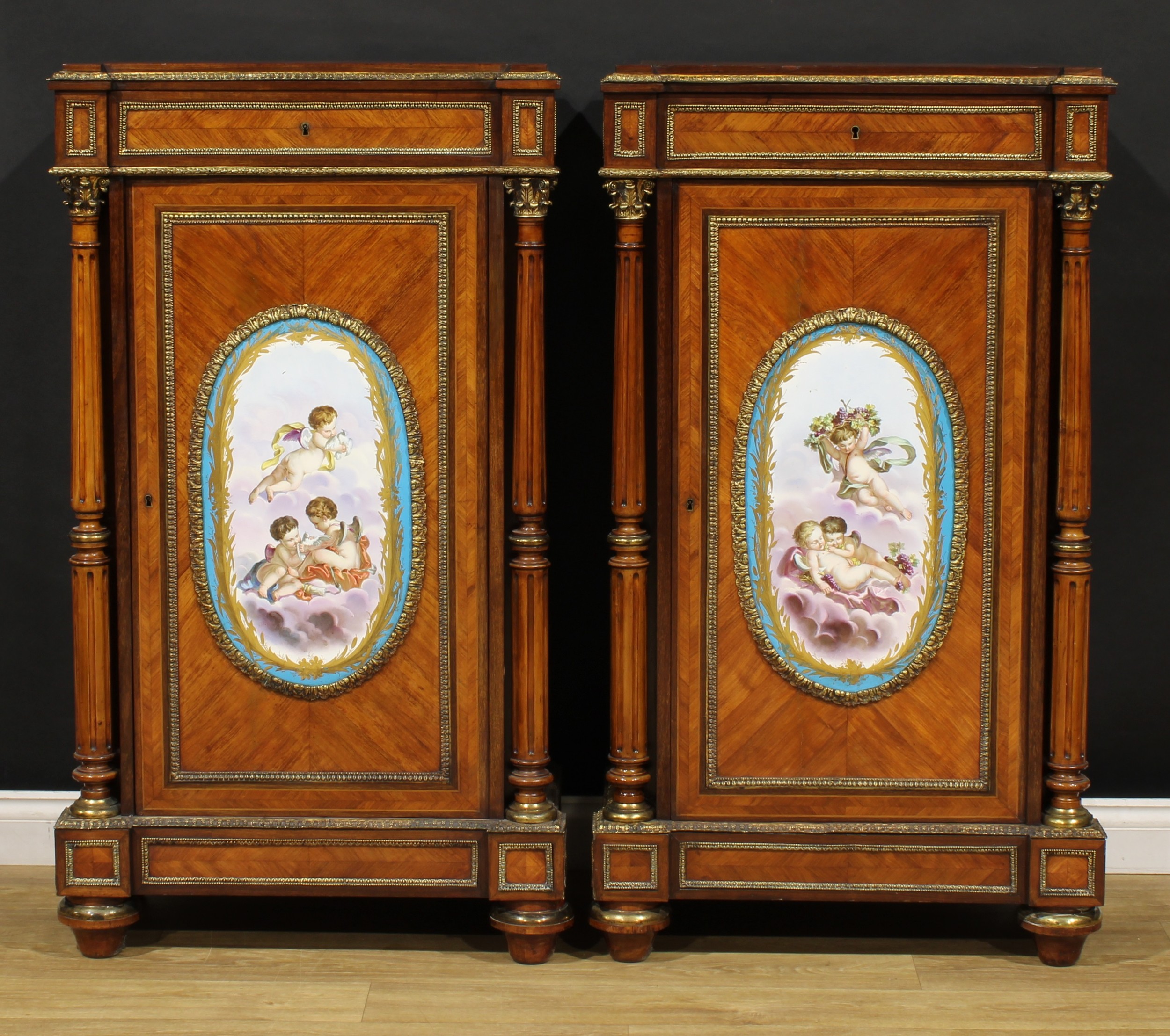 A pair of Louis XVI Revival gilt metal and porcelain mounted kingwood pier cabinets, each quarter-veneered top above a frieze drawer, the doors centred by a large panel painted in the manner of Sèvres, flanked by turned and fluted pillars, turned feet, 132cm high, 72cm wide, 38.5cm deep, c.1880