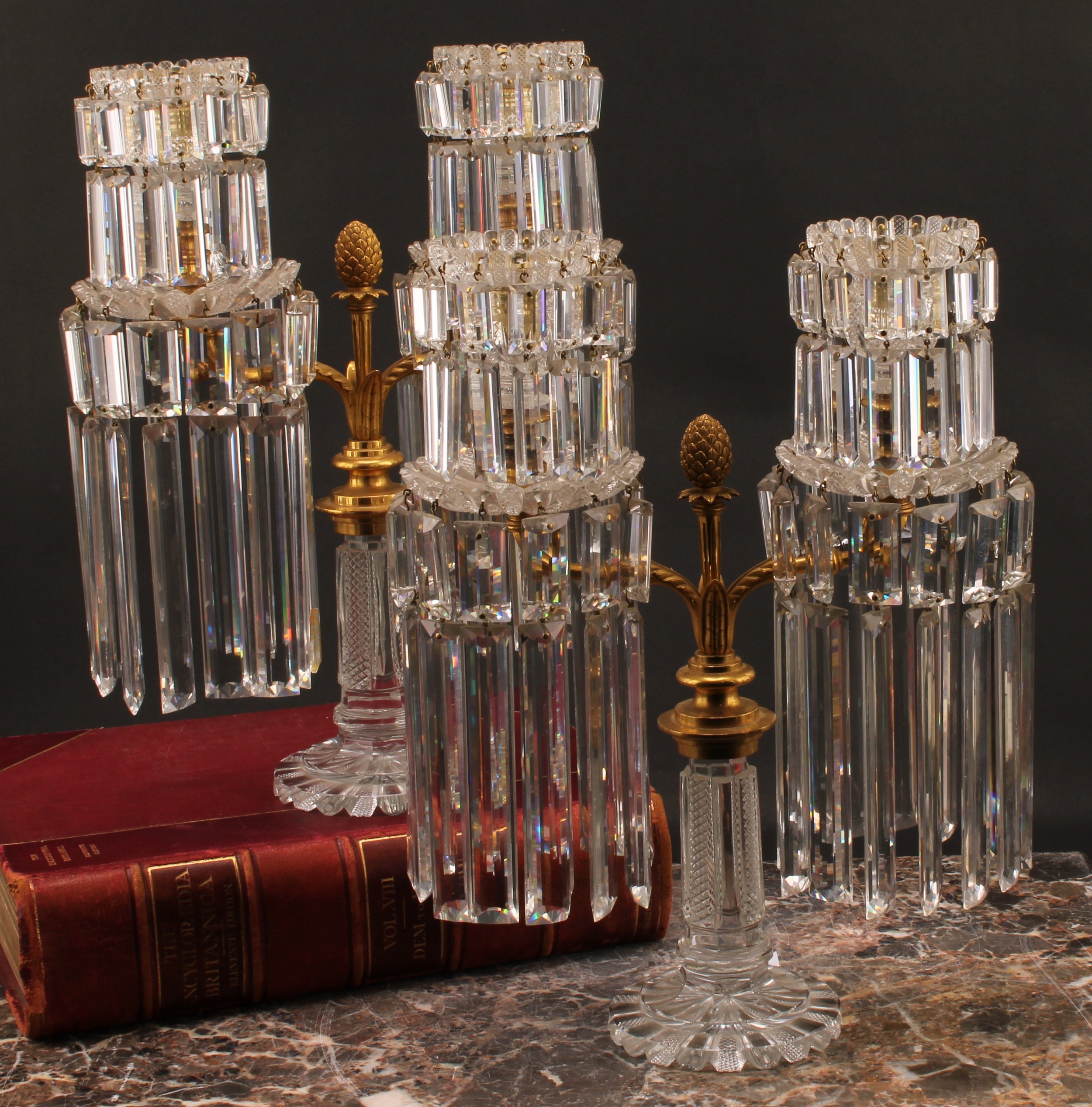 A pair of Regency gilt brass and cut glass two light table lustre candelabra, each branch fitted with two tiers of double bevelled rectangular glass droplets, the supporting pillars, bases and drip pans decorated with alternating clear and diamond patterned radiating panels, 35cm high, 26.7cm wide,  provenance from Earl of Favershams estate and Victoria & Albert Museum, M.63.i, c.1830