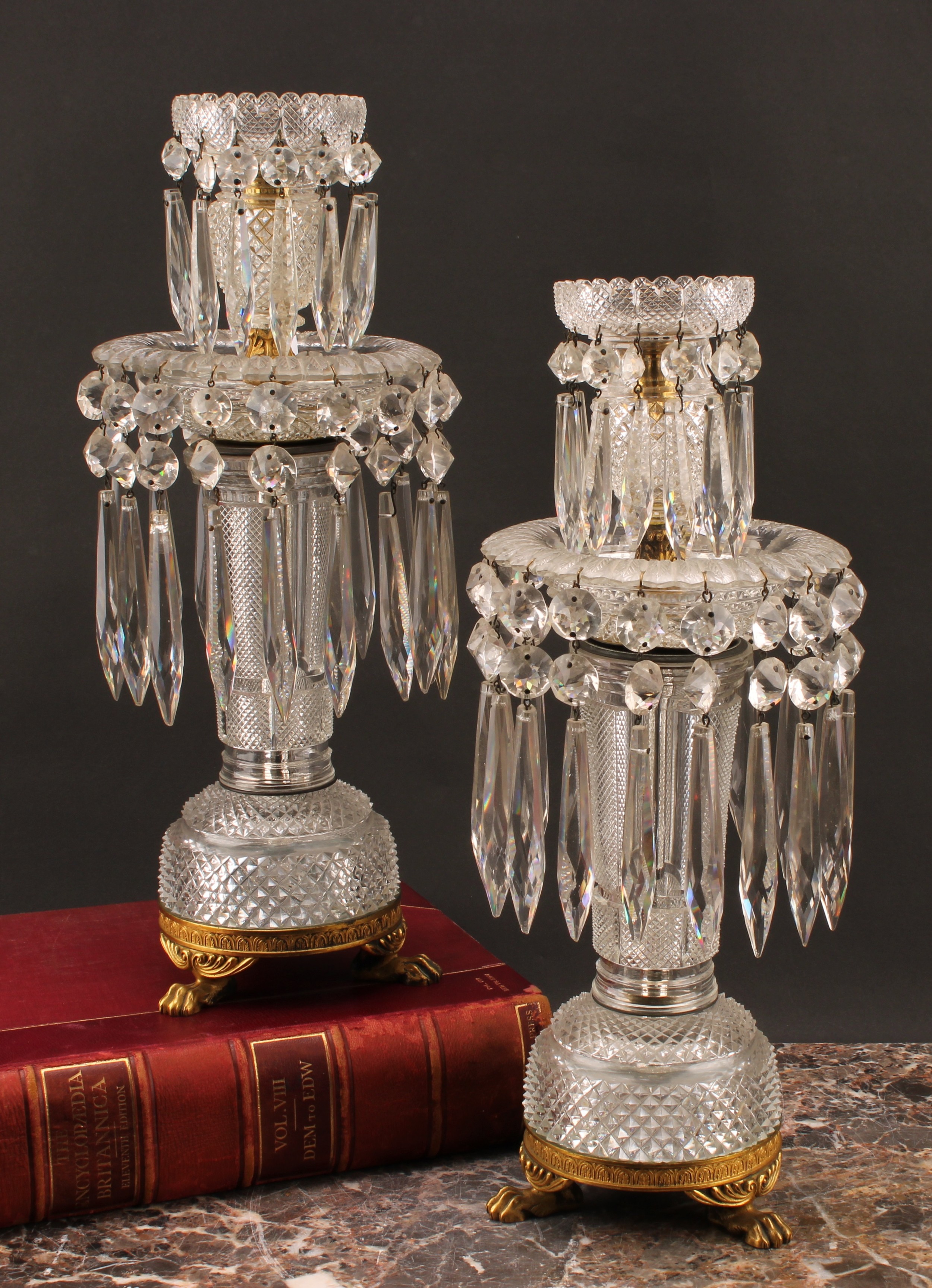 A pair of 19th century ormolu and cut glass mantle candlesticks, each with hobnail cut two section tops, tapering columns, hung with two rows of graduated cut glass droplets one to each level, raised on ormolu paw feet, 41.7cm high (2)
