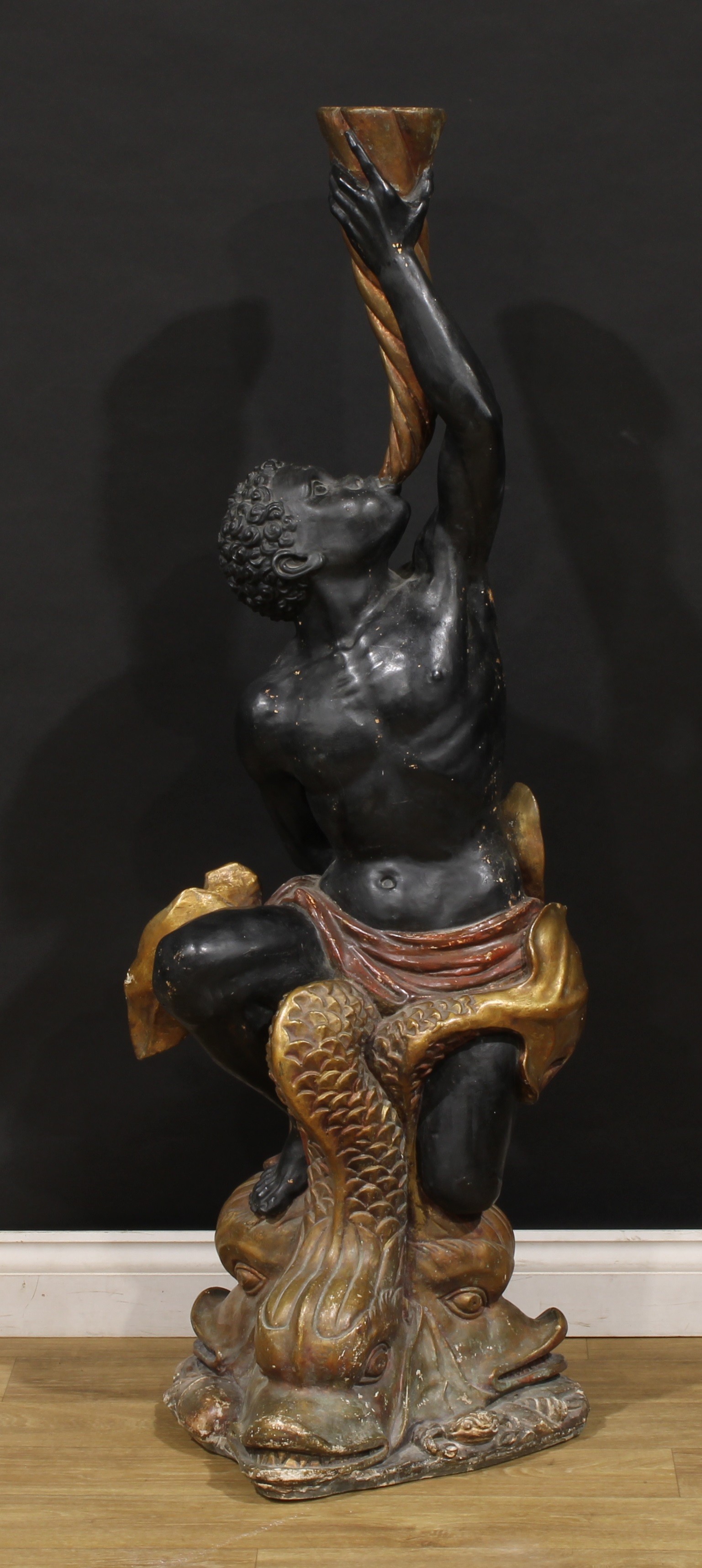Interior Design - a composite blackamoor torchère, in the 18th century Venetian taste, as a Nubian sounding a goat's horn, seated atop a triform arrangement of stylised dolphins, 137.5cm high