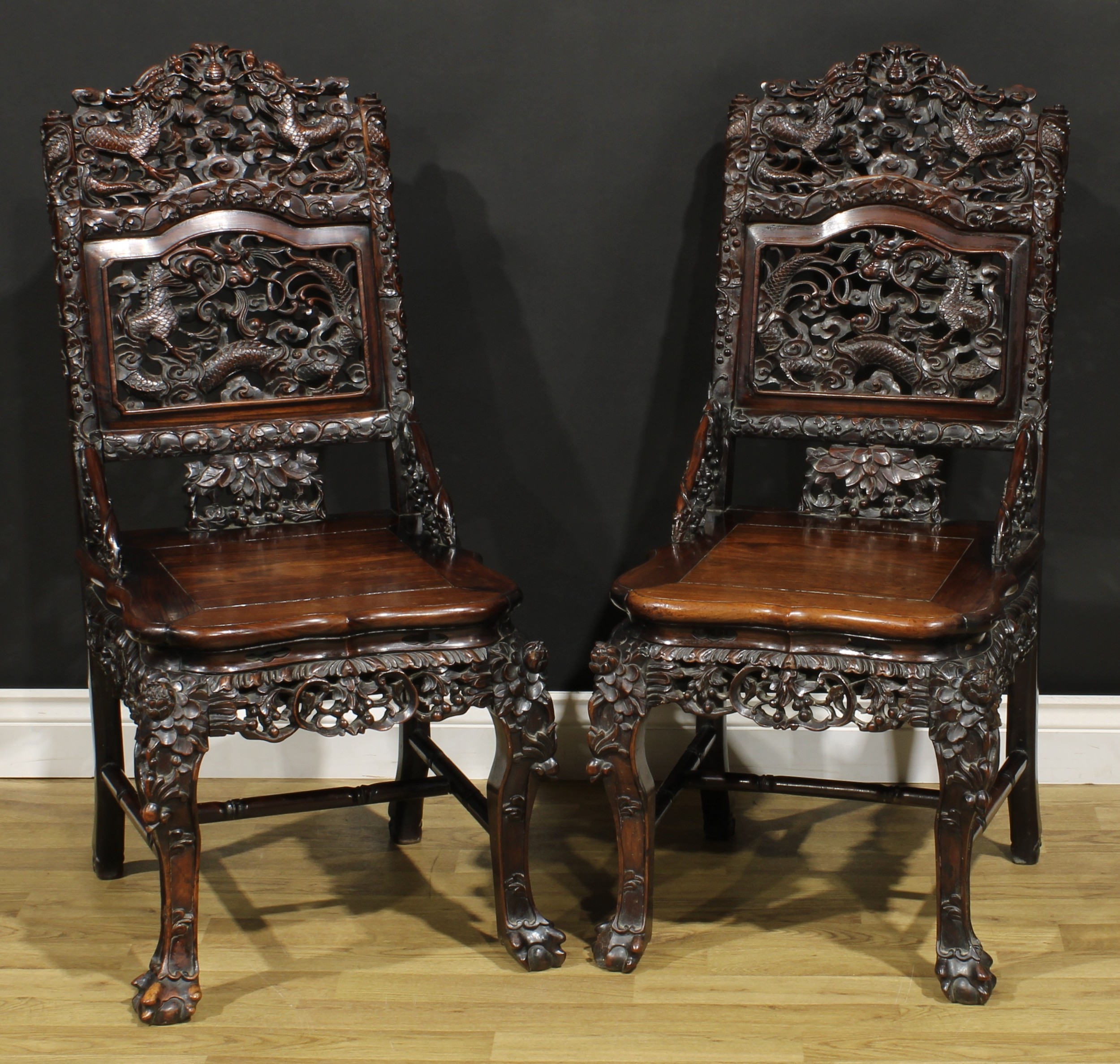 A pair of Chinese hardwood chairs, each with a shaped cresting pierced and carved with two dragons centred by a flaming pearl, the central panel depicting the victor, panel seat, the apron pierced and carved with fruiting branches, cabriole forelegs, H-stretcher carved as leafy bamboo, ball and claw forefeet, 99.5cm high, 47.5cm wide, the seat 37cm wide and 42cm deep