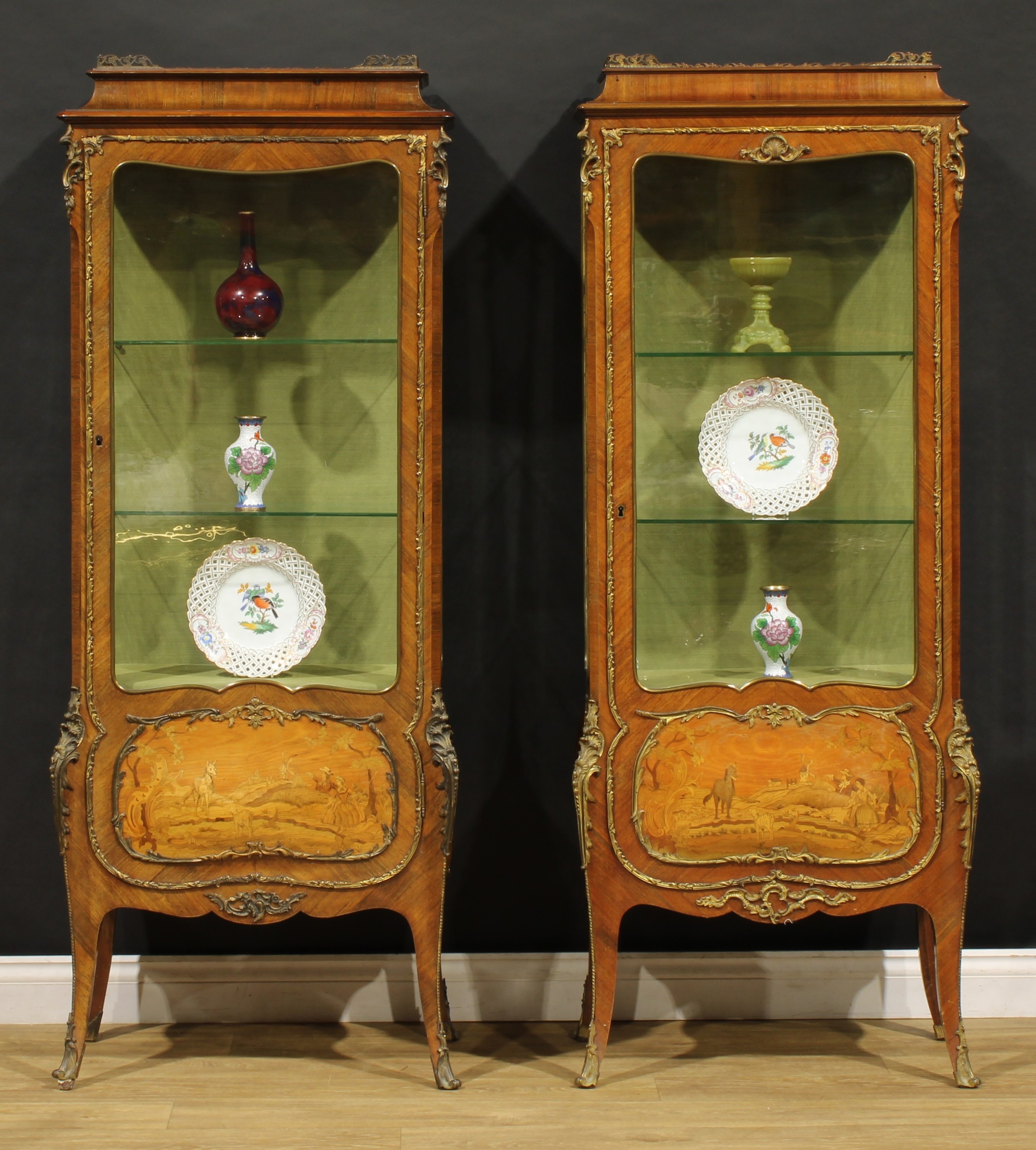 A near pair of French gilt metal mounted kingwood and marquetry vitrines, each with pierced gallery above a three-quarter glazed door enclosing shelves, the lower sections inlaid with pastoral idylls, 168.5cm high, 64cm wide, 36.5cm deep, late 19th century
