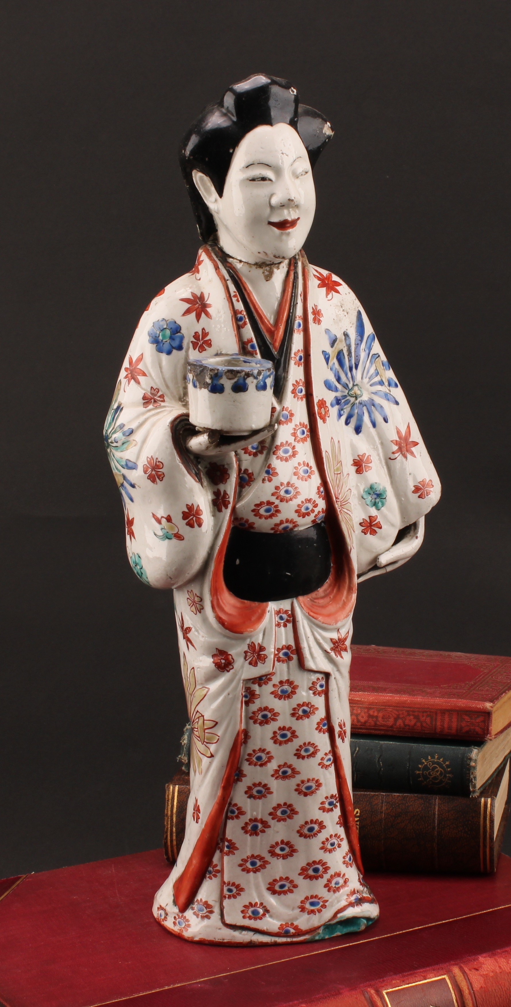 A Japanese Kakiemon porcelain figure, of a bijin, she stands, holding a koro or vessel, her kosode painted with flowers in tones of iron red, blue, green, and yellow, 42.5cm high, Edo period, c.1690