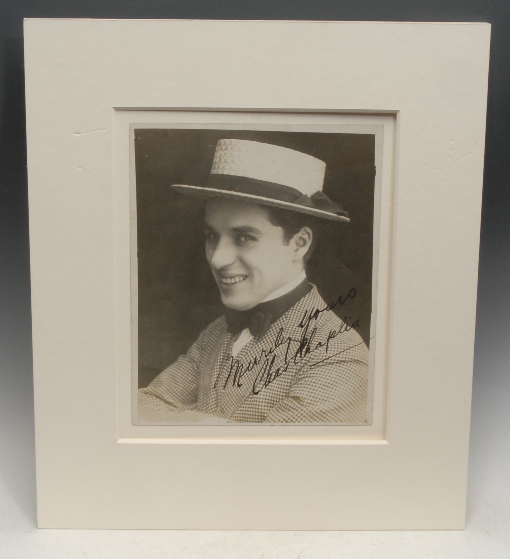 Autographs & Hollywood Golden Age - Portrait of Charlie Chaplin (1889-1977), signed MERRILY YOURS CHARLES CHAPLIN in ink, 25.5cm x 20.5cm