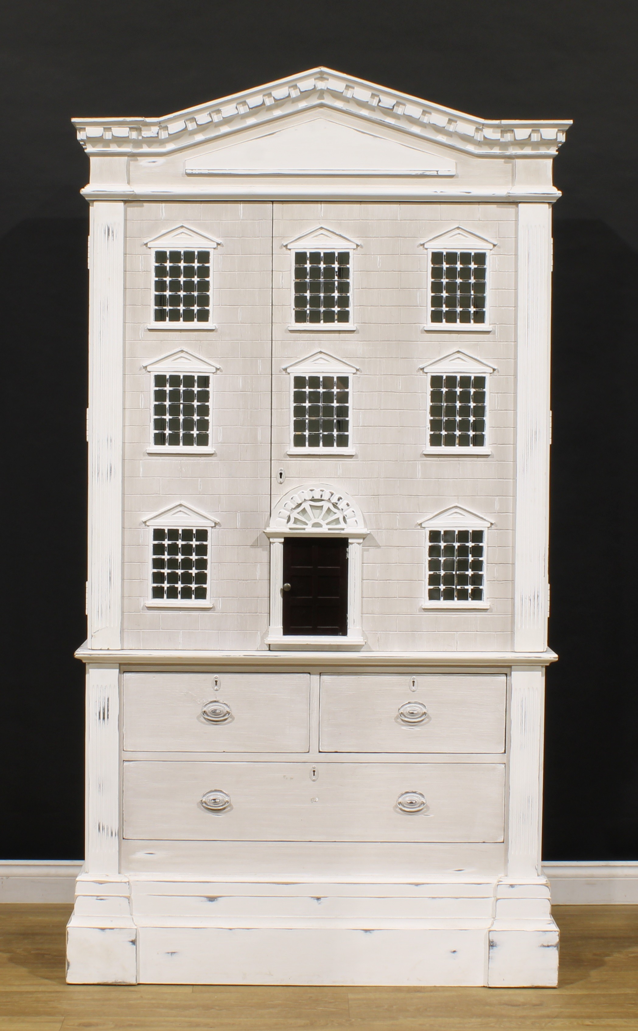 A contemporary 18th century style architectural doll’s house cabinet, by Andrew Martin, pointed dentil pediment above a hinged faux-rusticated facade enclosing two adjustable shelves, the base with two short and two long drawers, 215.5cm high, 116cm wide, 45cm deep