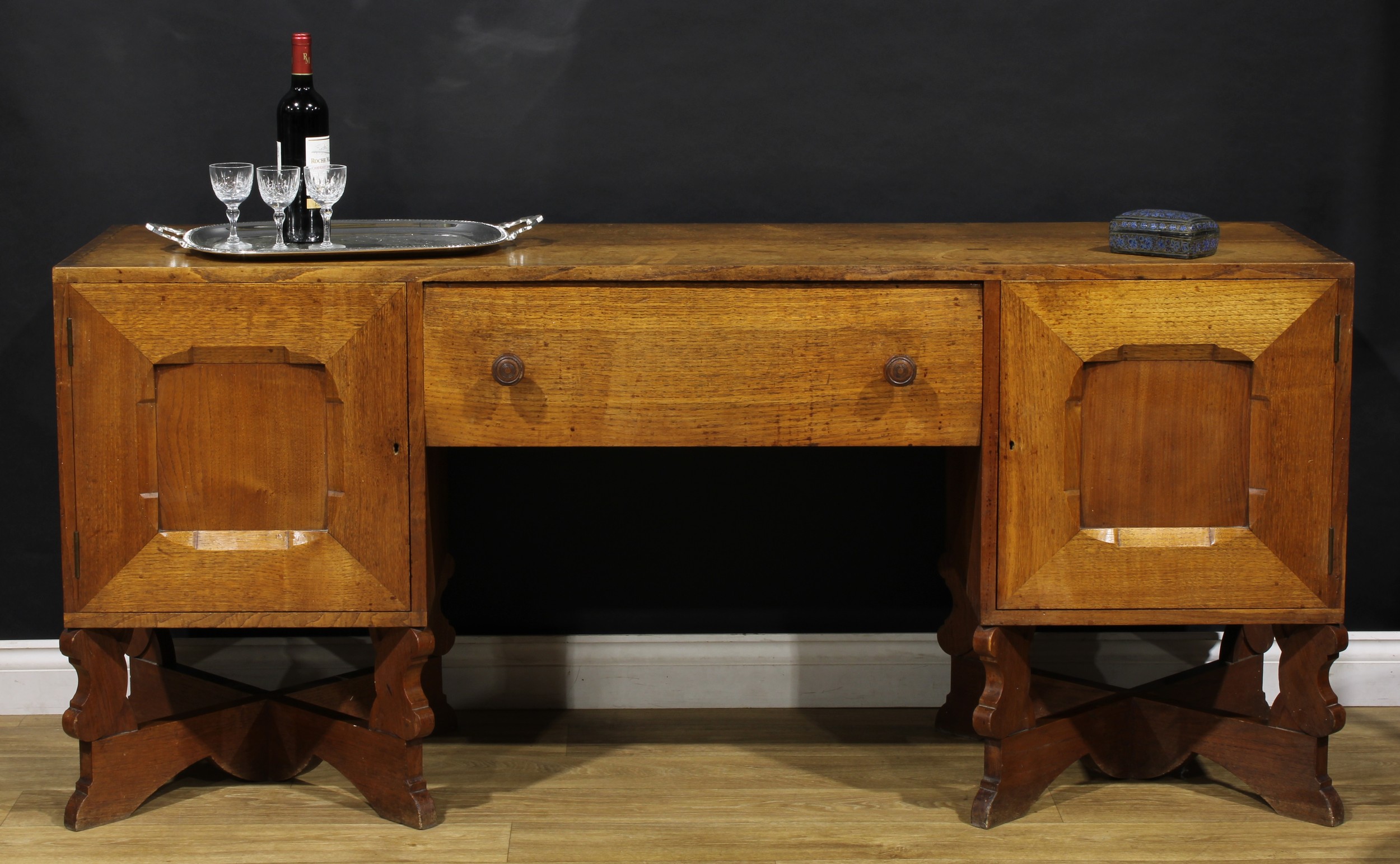 An Arts & Crafts oak sideboard, by Arthur Romney Green (1872-1945), flush rectangular top above a central frieze drawer flanked by panel doors, each enclosing a shelf, 79.5cm high, 178cm wide, 50cm deep, c.1920