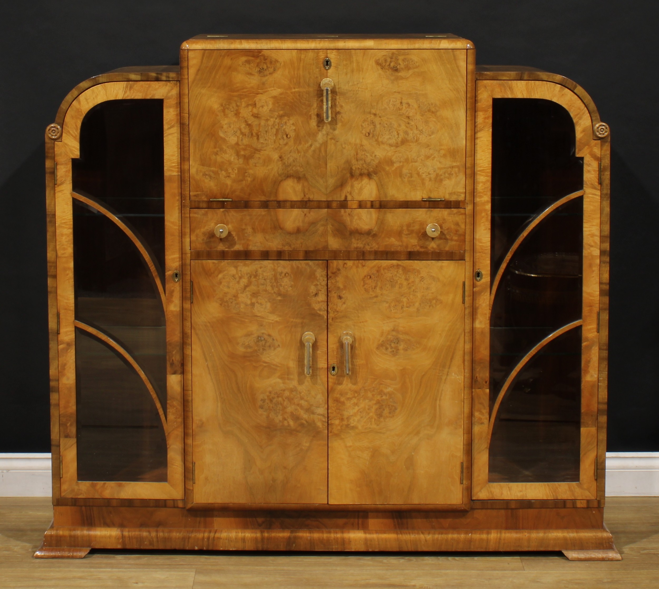 An Art Deco walnut drinks or cocktail cabinet, fall front above a central door and two doors flanked by glazed vitrine doors, bracket feet, 125cm high, 141.5cm wide, 42cm deep, c.1930