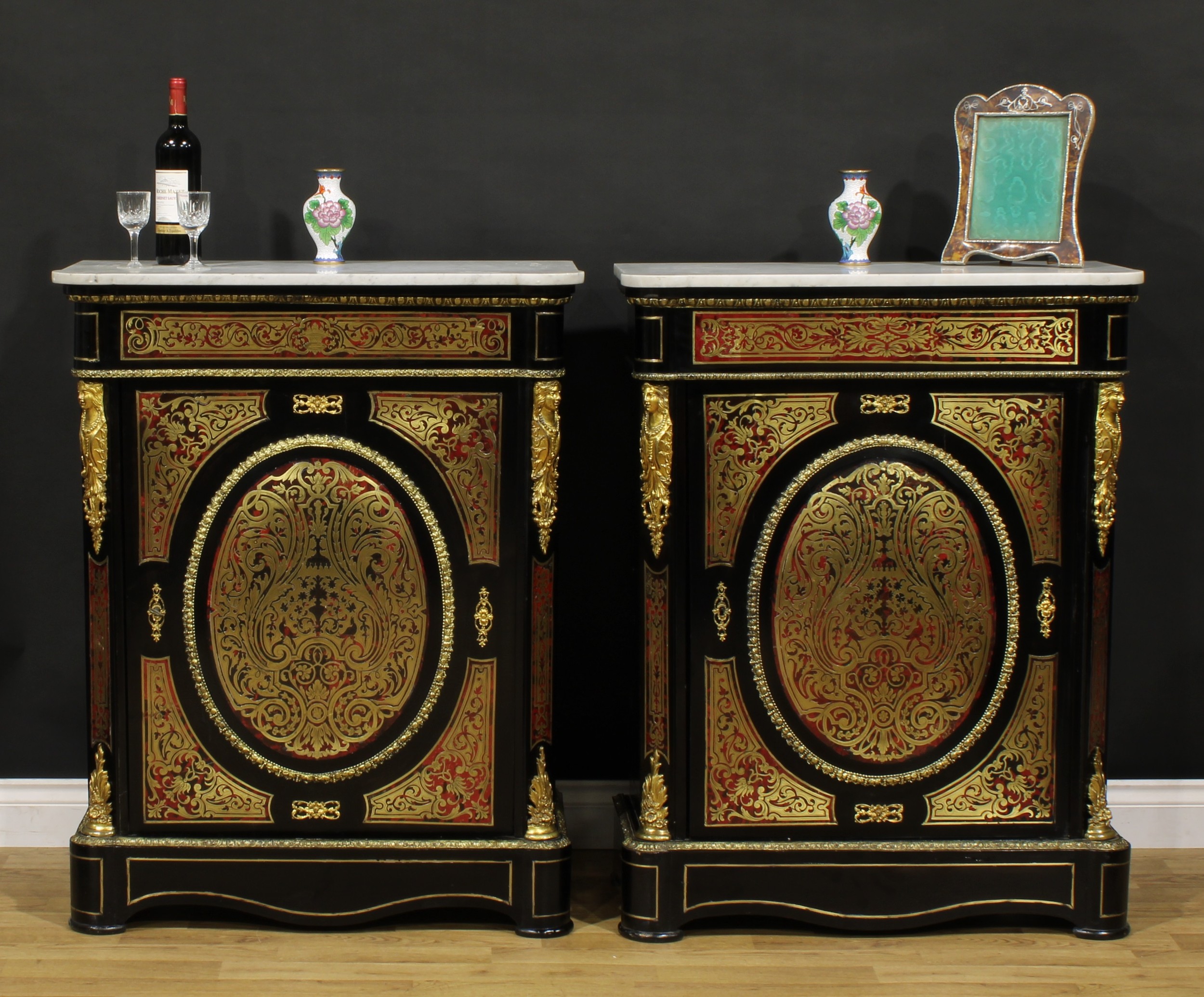 A near pair of Louis XV Revival gilt metal mounted, ebonised and premier and contra-partie brass marquetry pier cabinets, in the manner of André-Charles Boulle, each with a marble top above a door enclosing two shelves, the largest 105cm high, 83cm wide, 39cm deep, the other 105cm high, 81cm wide, 38.5cm deep, c.1880