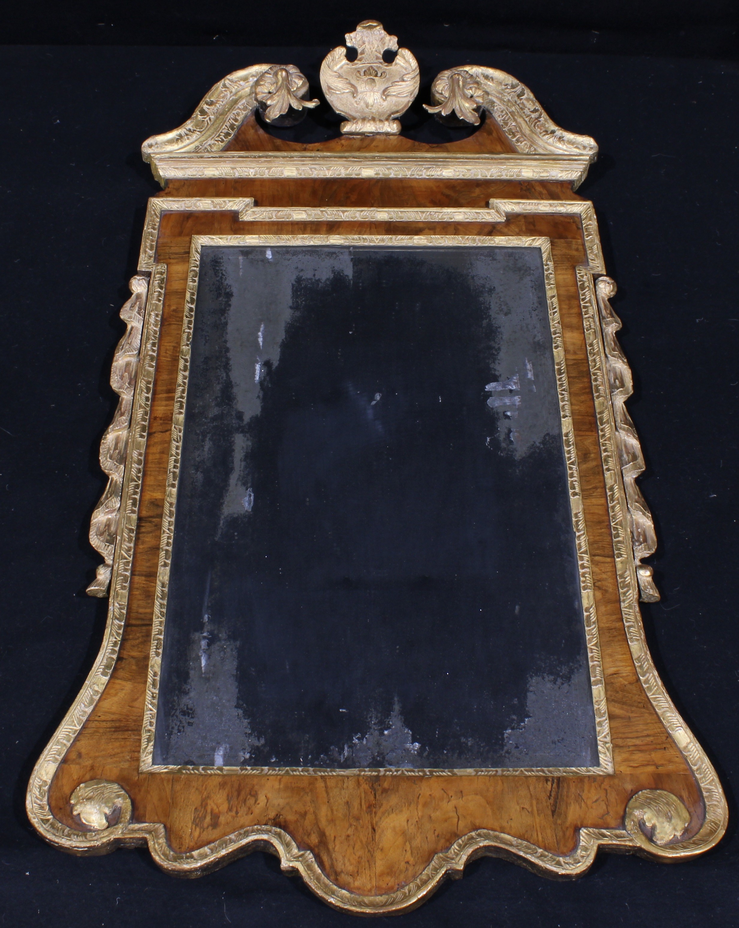 A George II walnut and parcel-gilt pier glass, in the manner of William Kent, bevelled rectangular mirror plate, the frame with swan neck pediment centred by a foliate cartouche, 129.5cm high, 68.5cm wide, c.1740