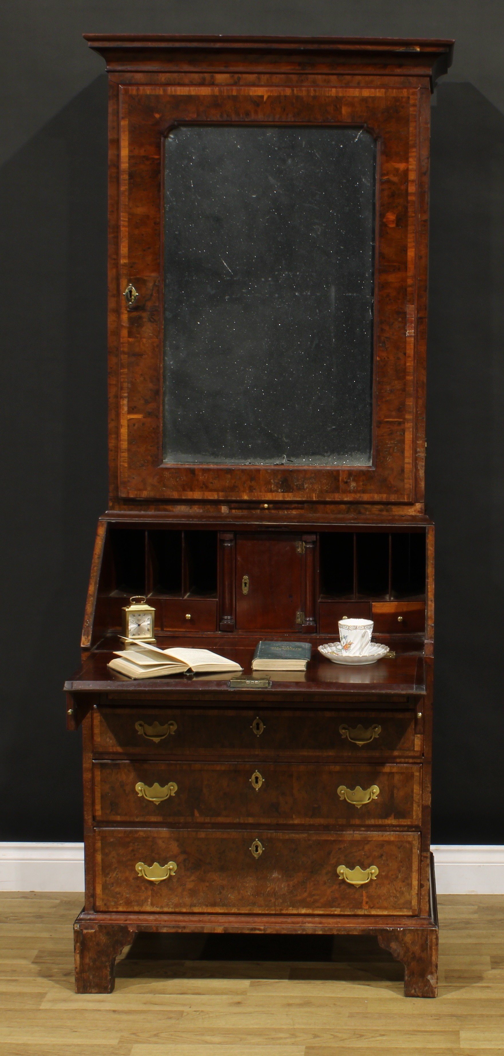 An 18th century burr yew bureau book cabinet, moulded cornice above a mirrored door enclosing a shelf and three small drawers, the projecting base with fall front enclosing a well, a small door, drawers and pigeonholes, above four long drawers, skirted base, bracket feet, 197.5cm high, 77cm wide, 52cm deep