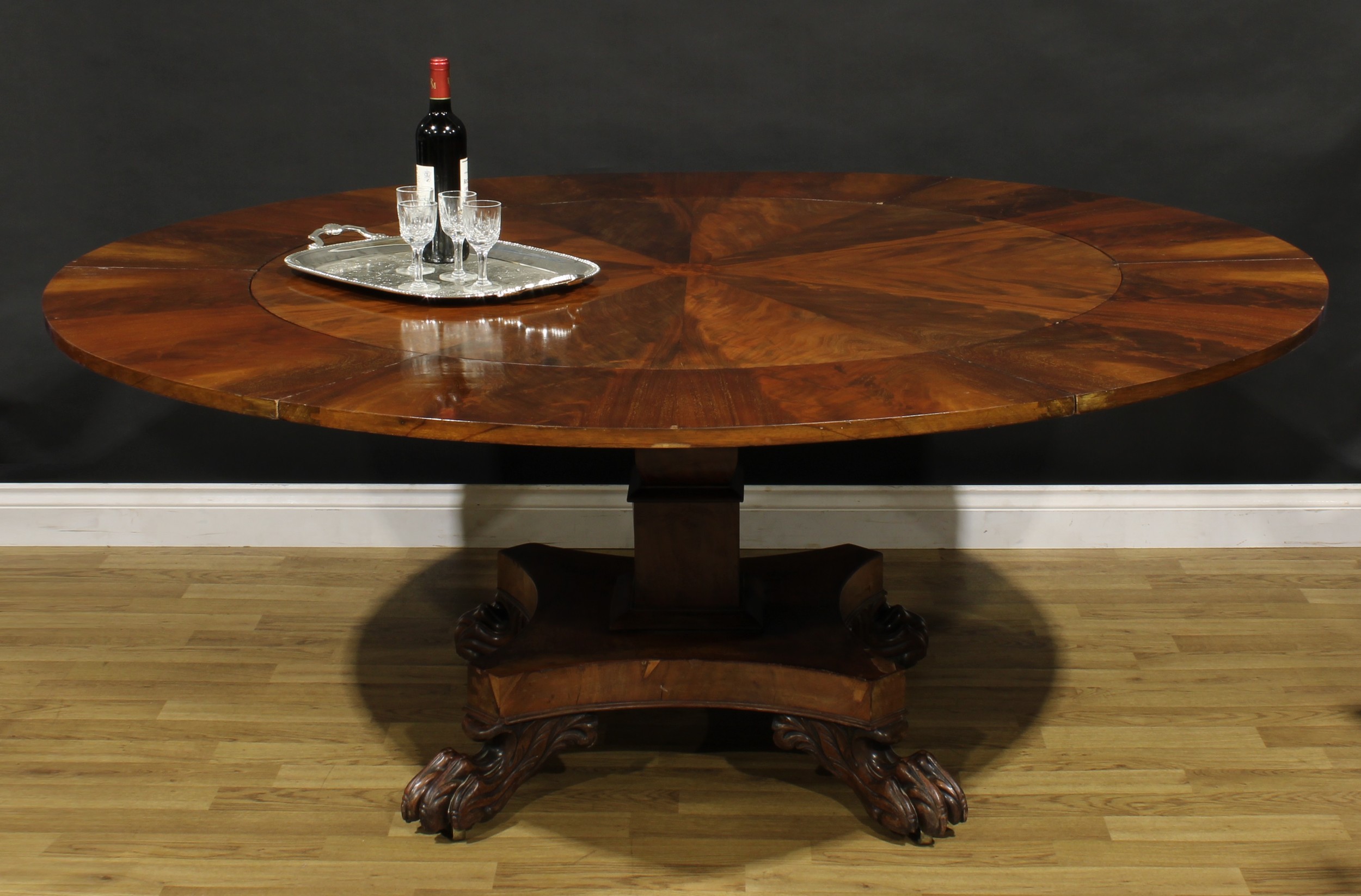 A William IV mahogany dining table, in the manner of Johnstone, Jupe & Co, circular top with segmented flame-veneers, six additional concentric leaves, incurve square base, paw feet, brass casters, 72.5cm high, 127.5cm extending to 183cm diameter, c.1835