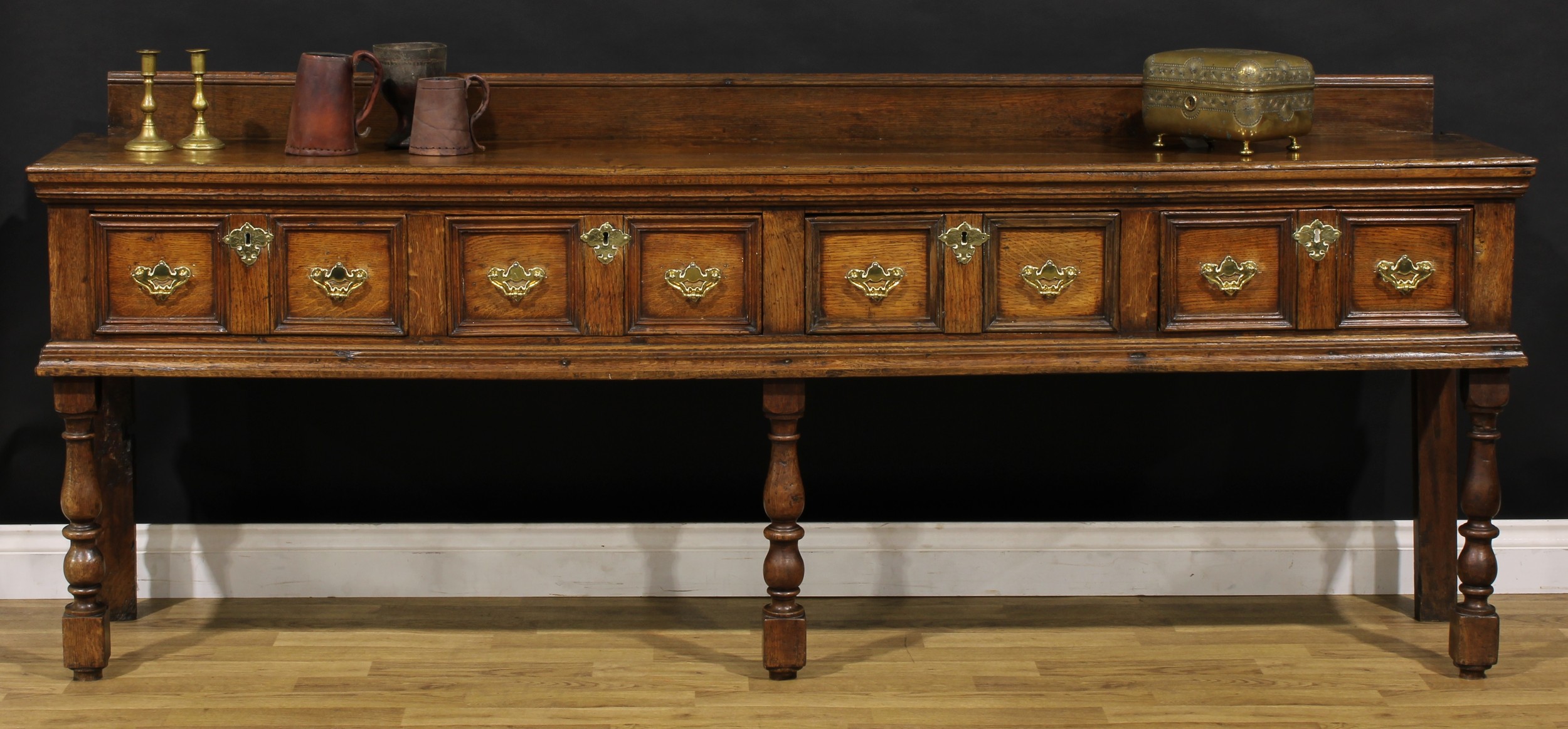 An early 18th century oak low dresser, rectangular top with moulded edge and half-gallery above four frieze drawers, brass swing handles, batwing backplates, turned and blocked forelegs, 86cm high, 216.5cm wide, 43cm deep